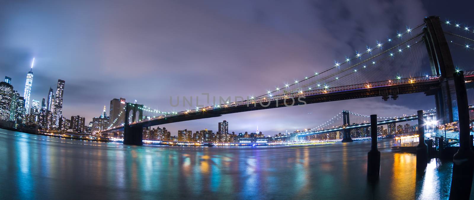 Manhattan bridge and New York City downtown skyline at dusk with skyscrapers illuminated over East River panorama. 