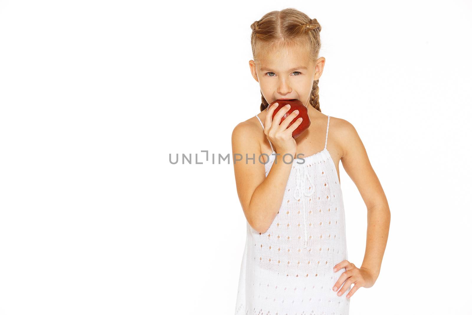 Cute little girl in a white dress bites red fresh apple