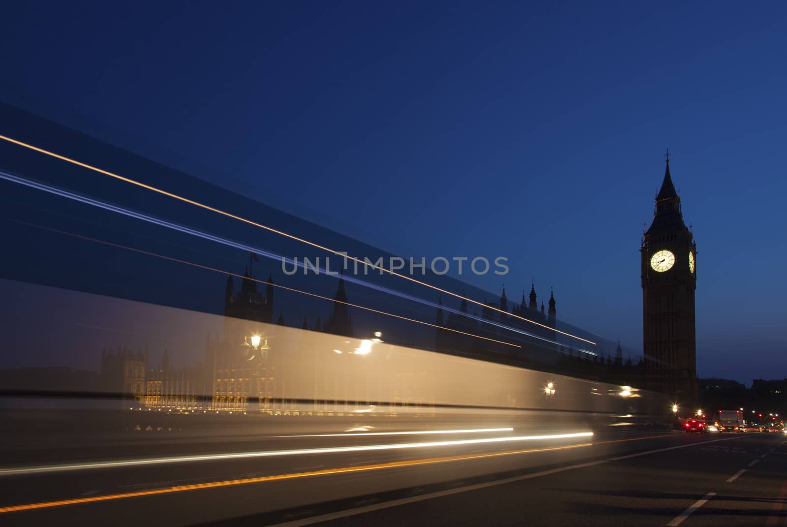 Night silhouette of Big Ben and light trail of a bus in front.