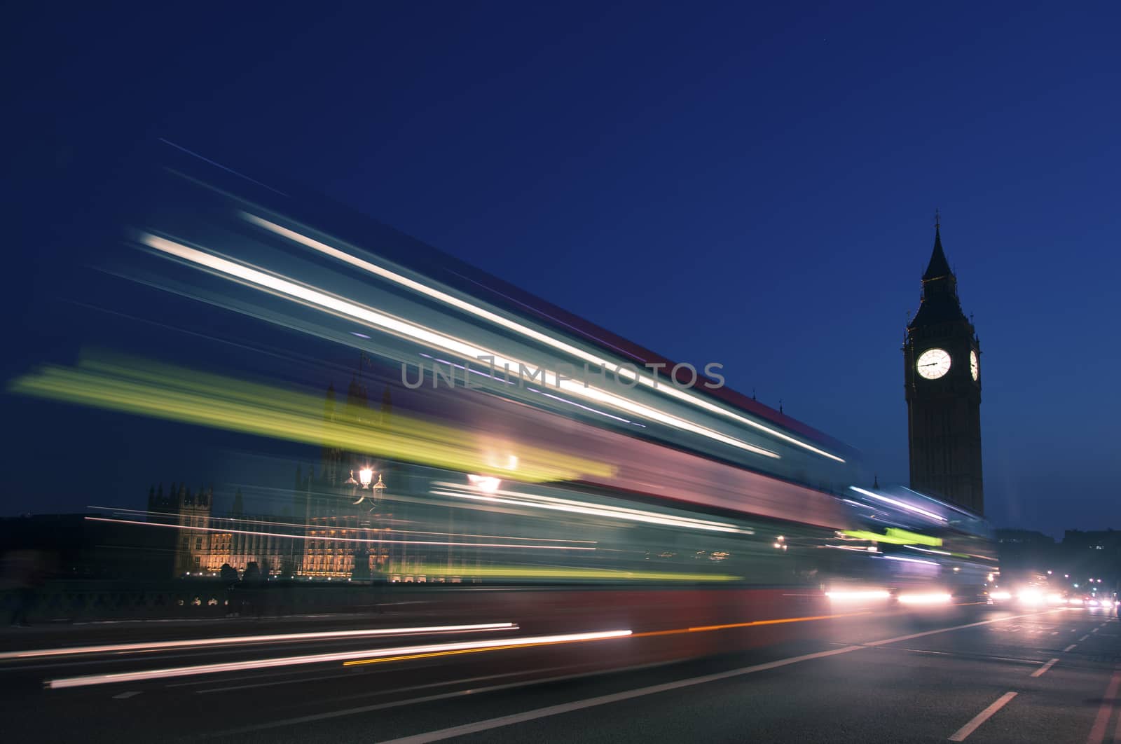 Night silhouette of Big Ben and light trail of a bus in front.