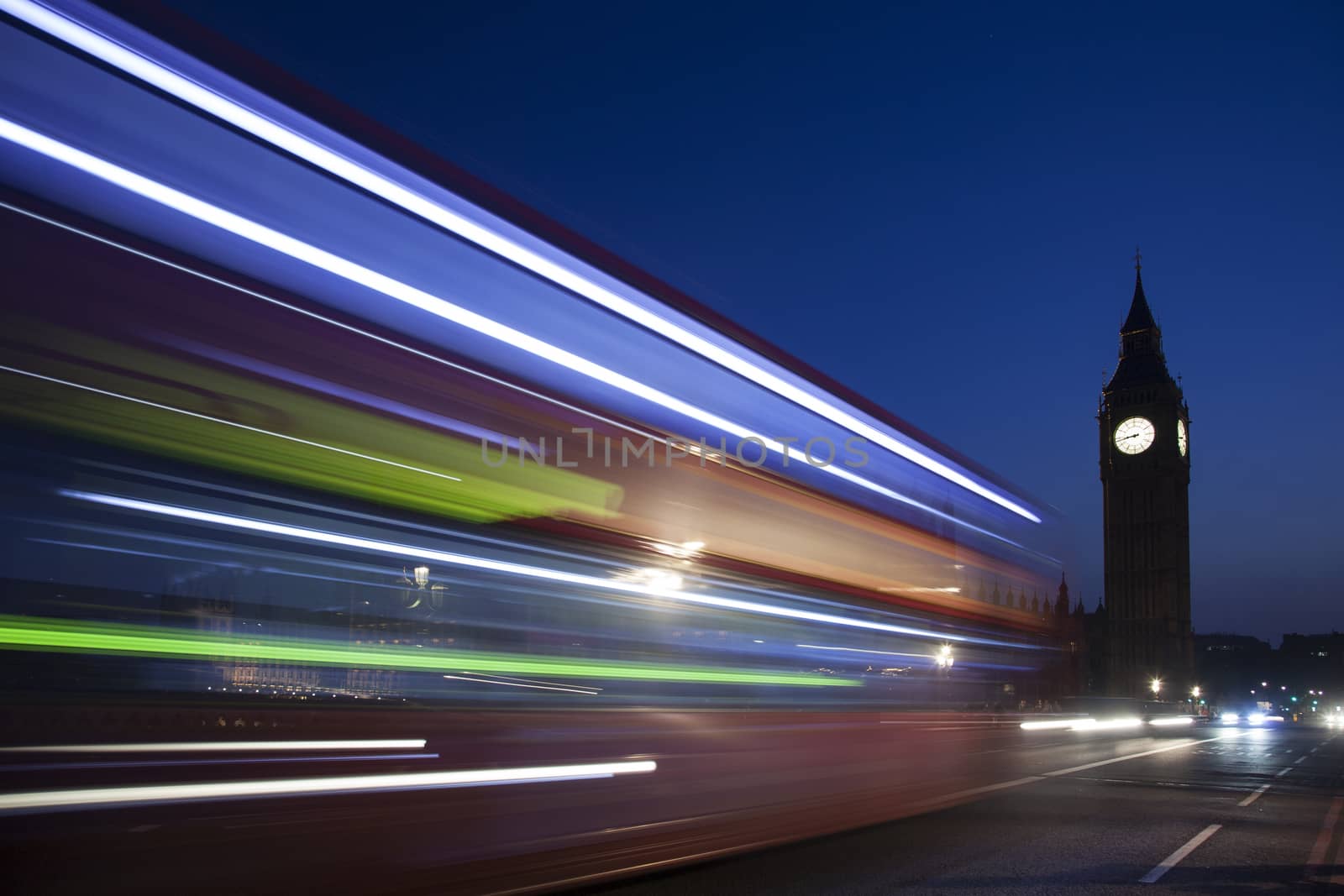 Night silhouette of Big Ben and light trail of a bus in front.