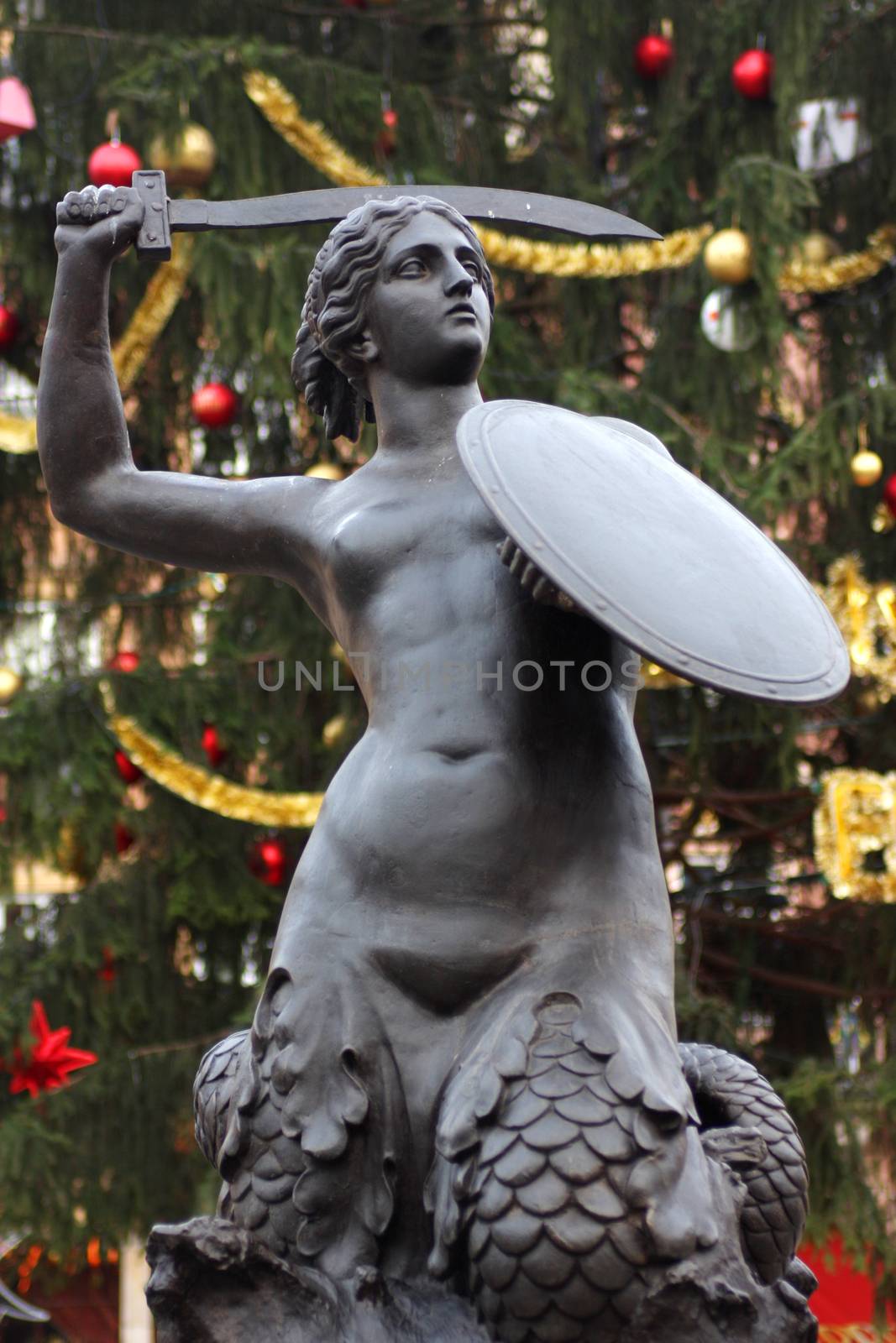 Syrenka statue in Old Town Market sqare in Warsaw with big Christmass tree in background. 