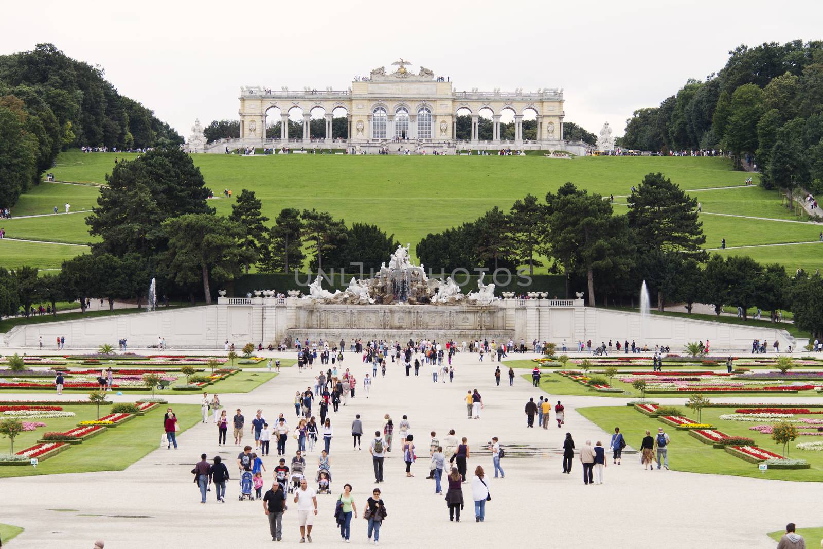 Vienna, Austria - August 17, 2010: The Gloriette, Neptune Fountain and gardens in front of Schonbrunn palace in Vienna, Austria. Beautiful gardens are often crowded with tourists from all over the world (on the picture).