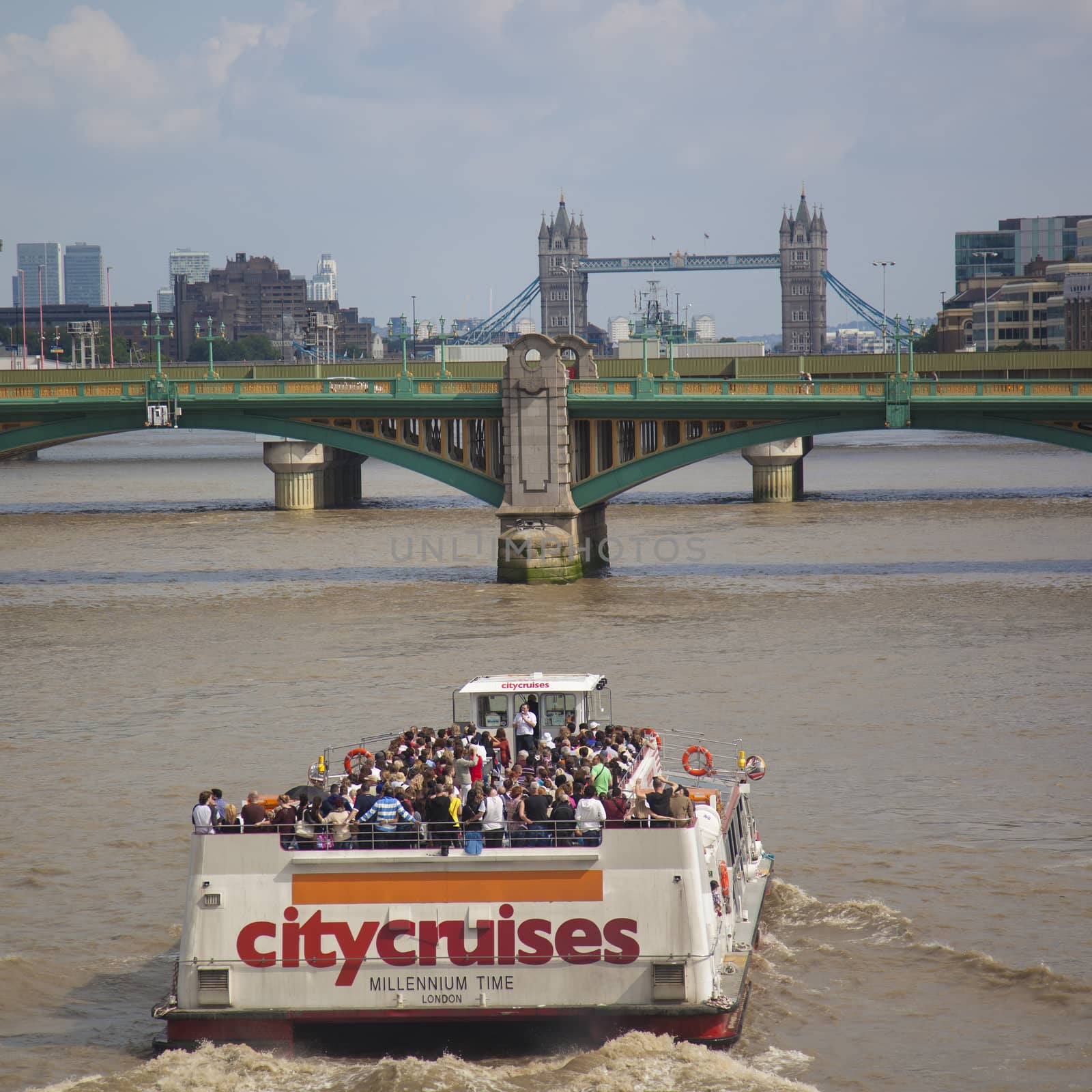 Tourists with boat on Thames River listening to their guide. London Bridge in background.