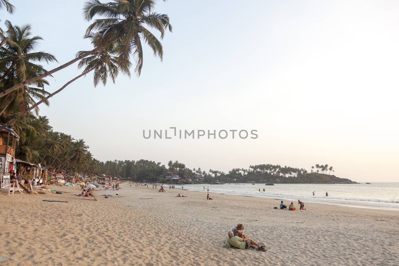 Palolem, India - January 4, 2013: Palolem beach in the south of Goa in India with coconut palm trees in the back. There mostly western tourists on the sand and coconut huts and restaurants in the back.