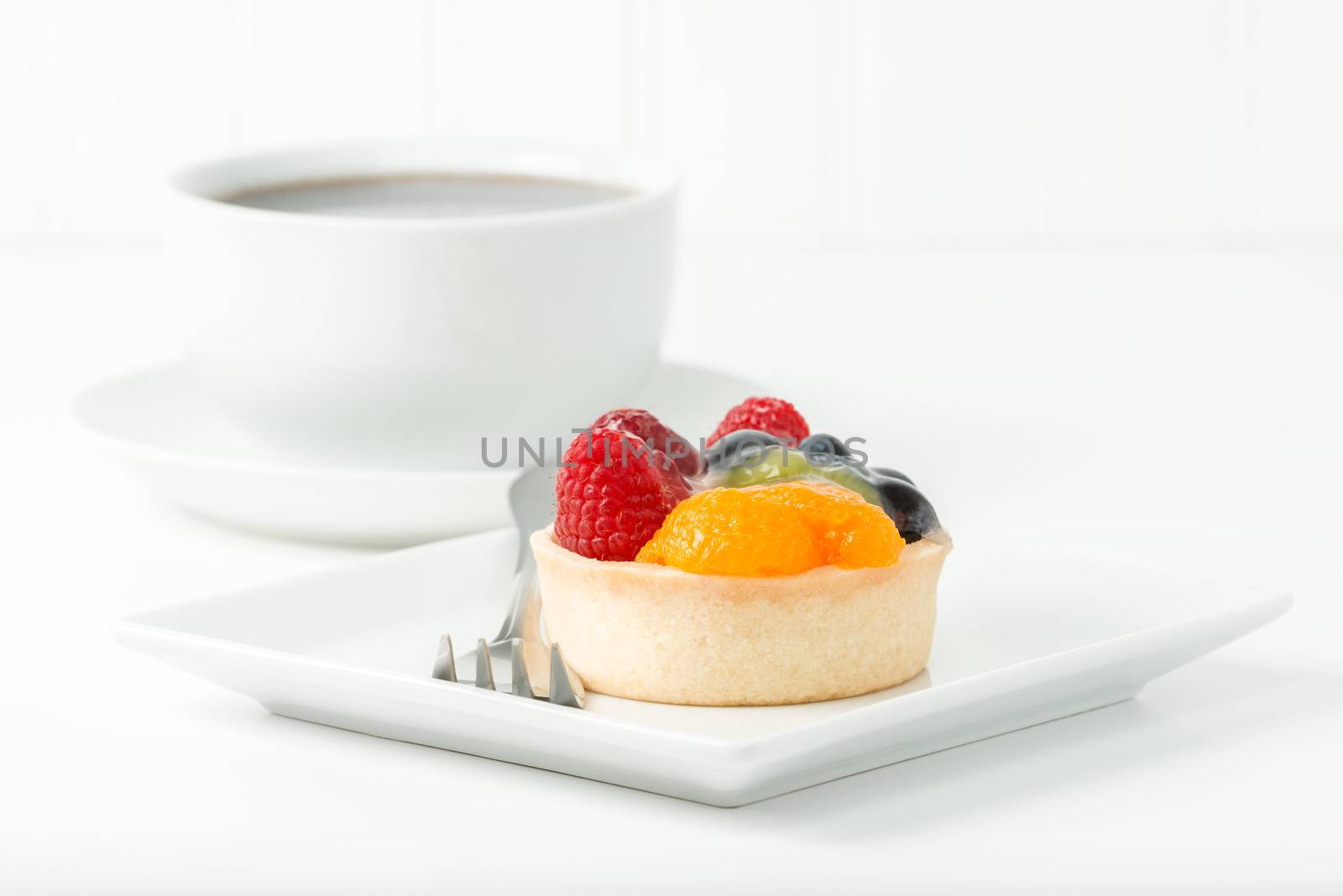 Colorful fresh fruit tart served with a cup of coffee.