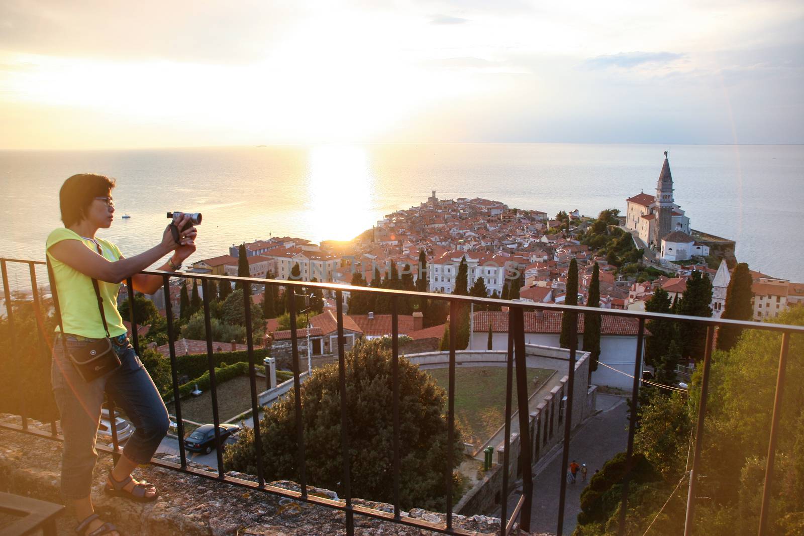 Girl with camera looking on a panoramic scene above Piran.