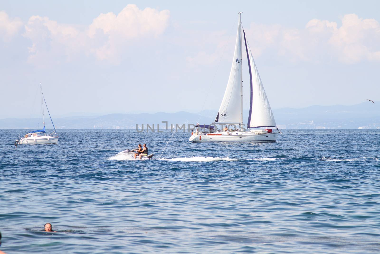 Yacht and people on water scuter by the coast.