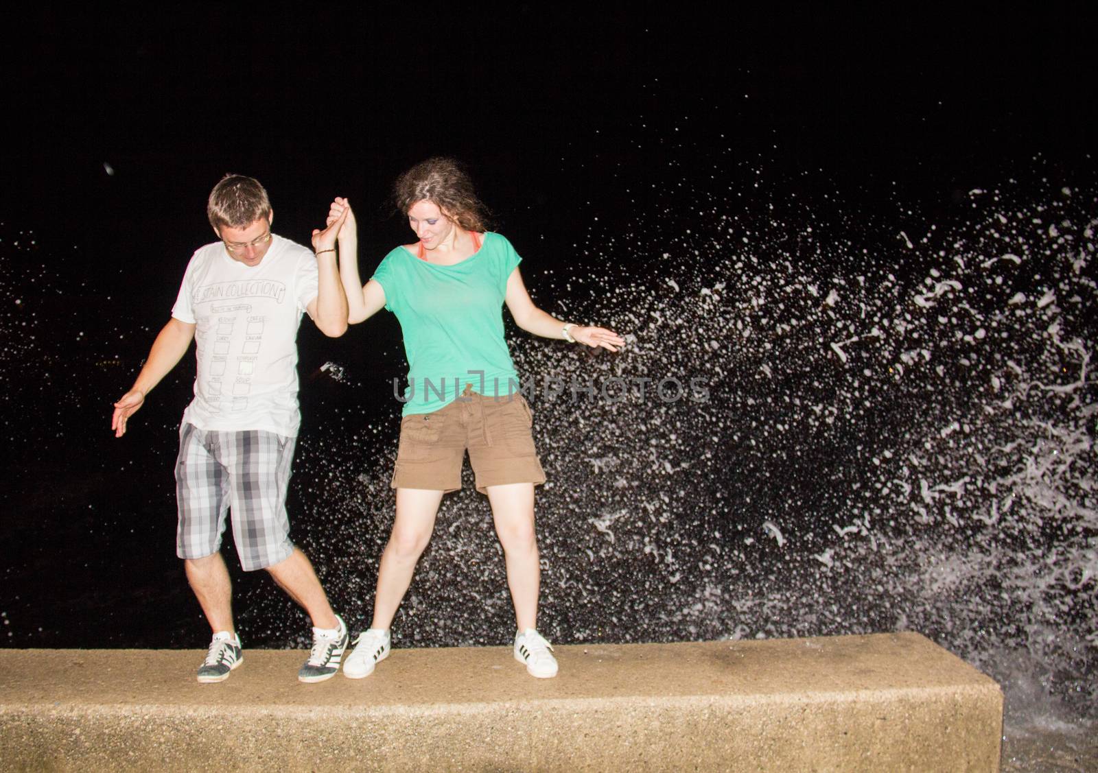 Young couple dancing on a pier with waves in the background.