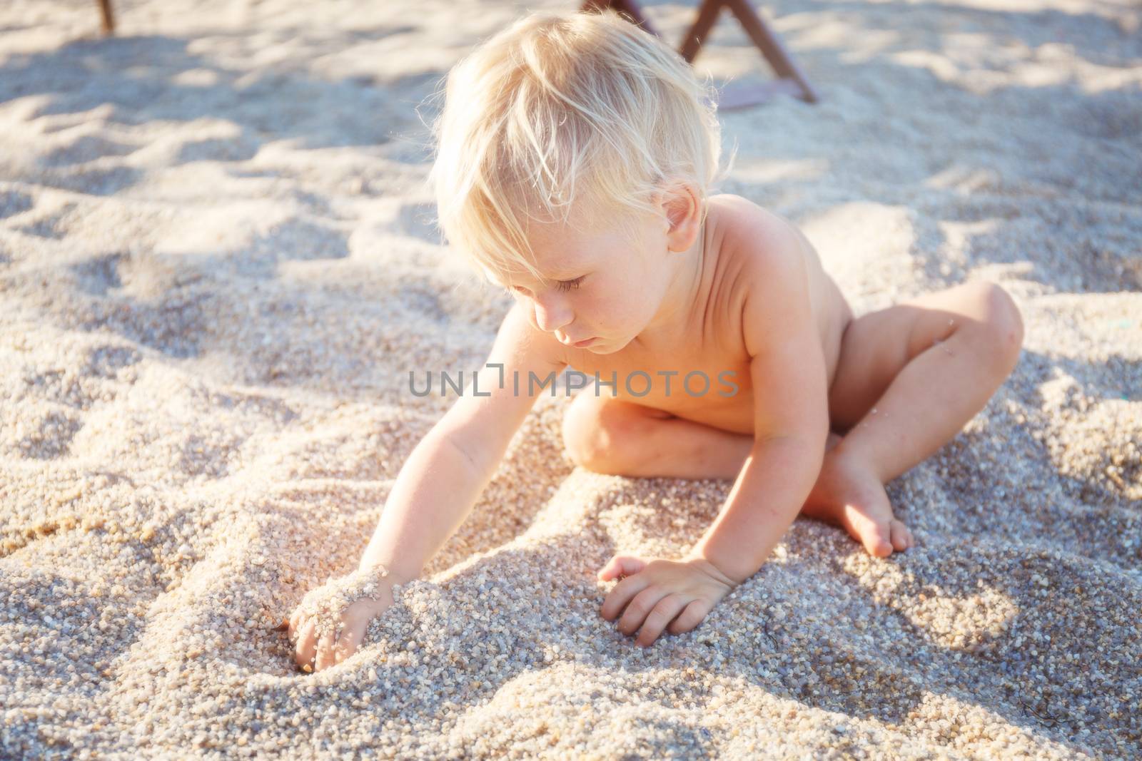 Little boy with blue eyes and white hair sitting on white sand 