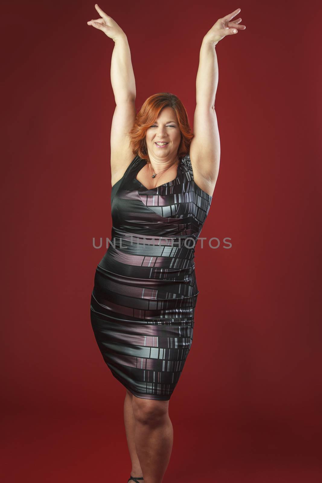 forty year old woman in cocktail dress, with her arms up in lady styling position