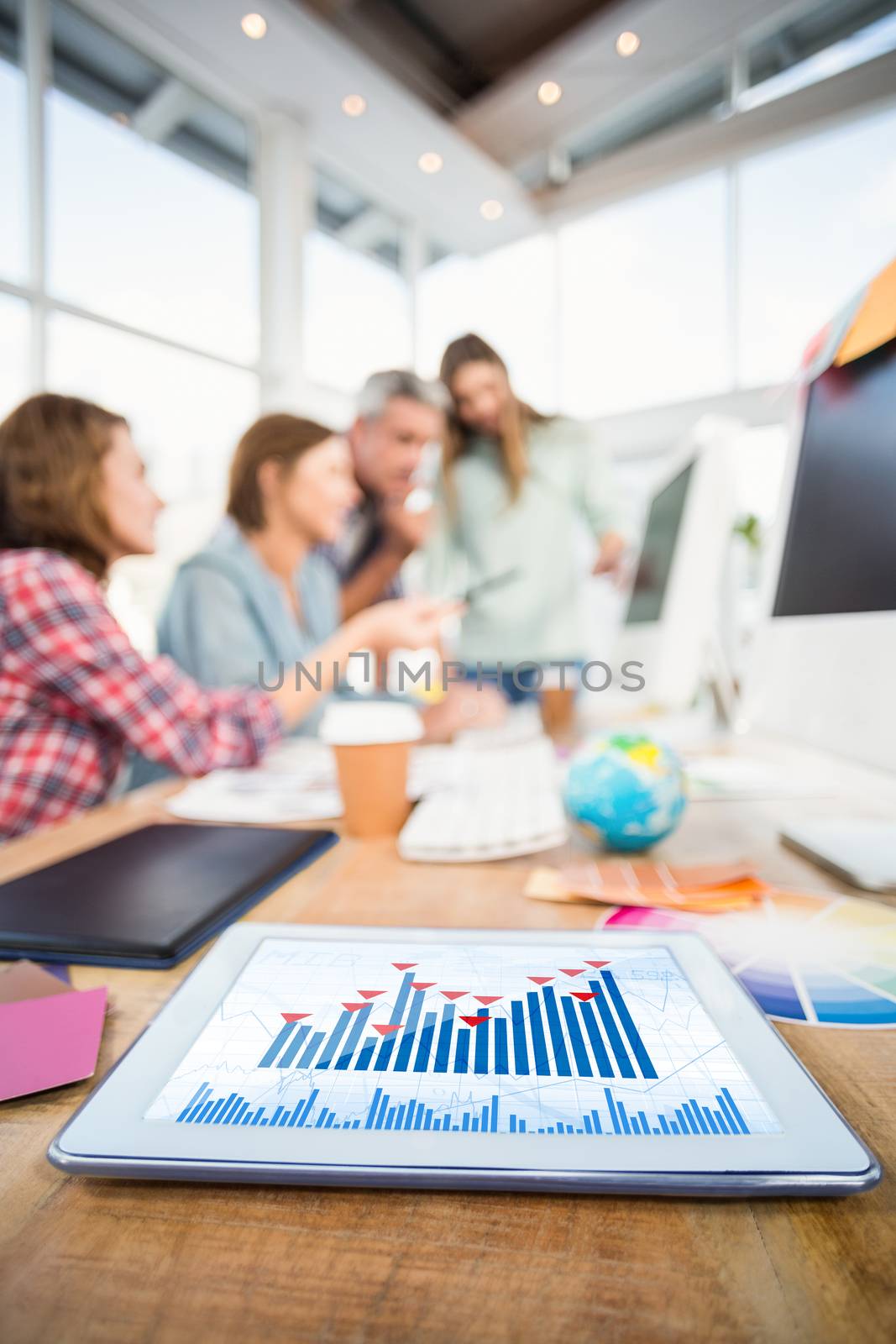 Blue data against tablet in the foreground with business people in the background 