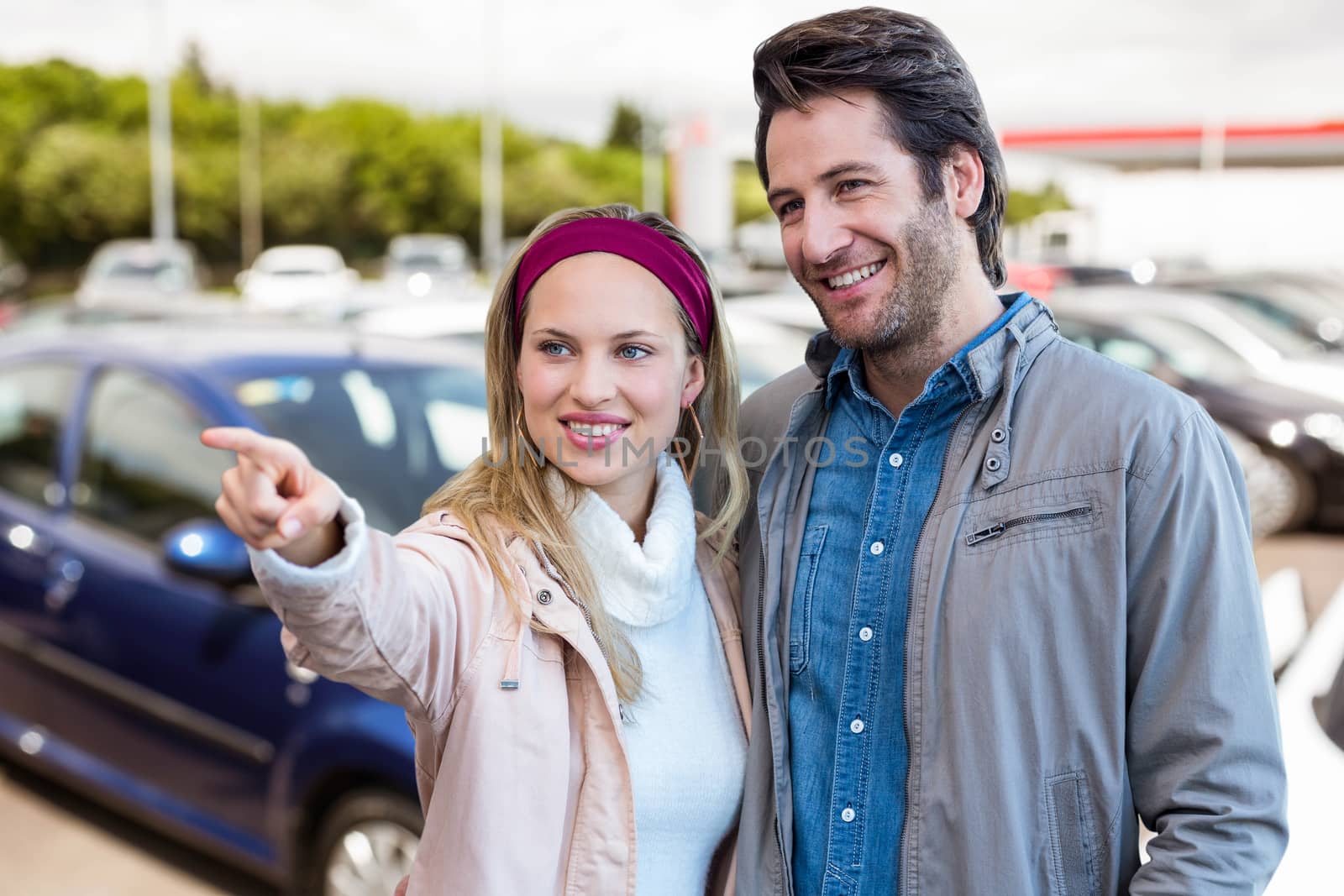 Smiling couple looking and pointing against view of row new car 