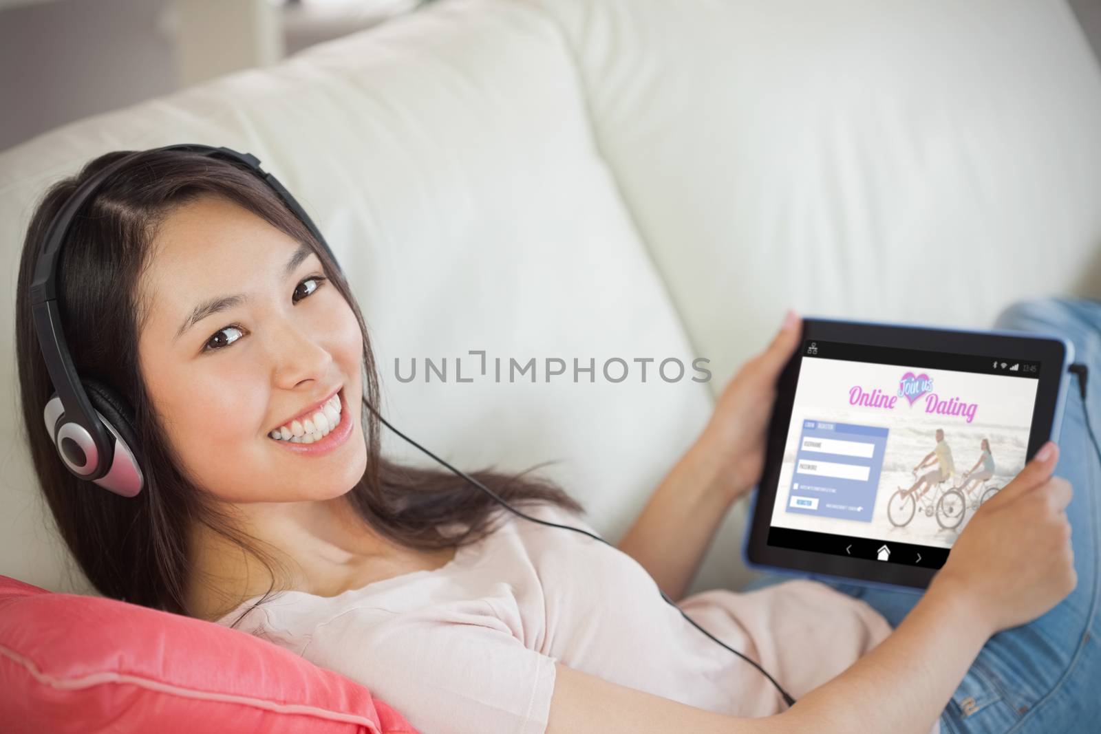 Girl using her tablet pc on the sofa and listening to music smiling at camera against online dating app