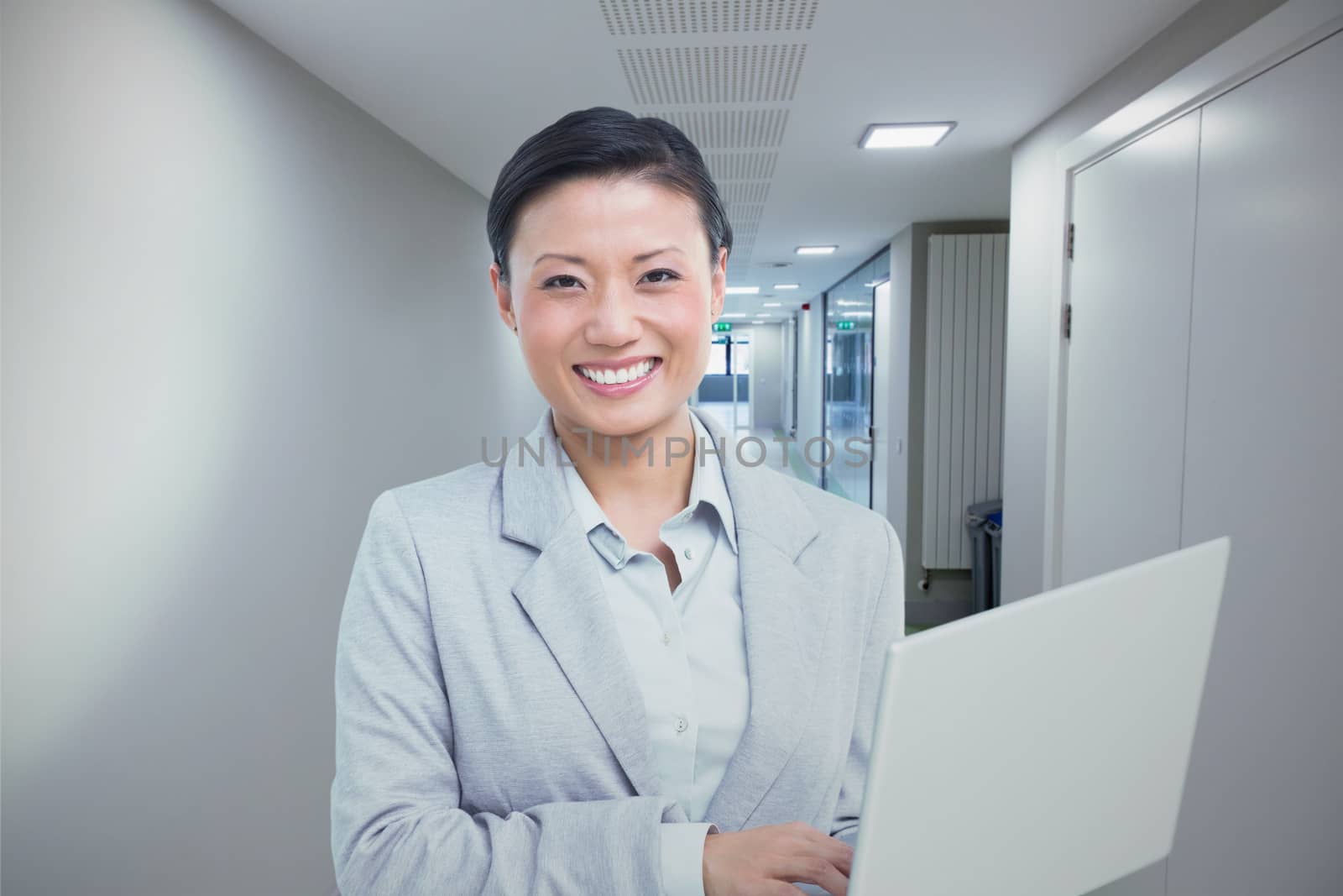 Businesswoman using laptop with colleagues behind against college hallway