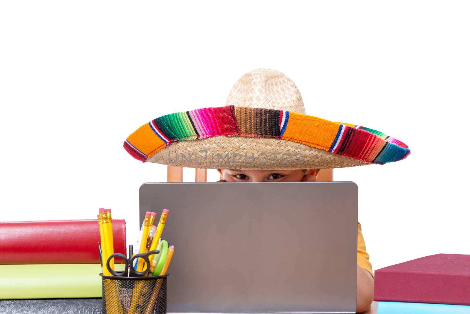 Partially hidden face of child in large colorful sombrero with laptop surrounded by books and pencils over white background