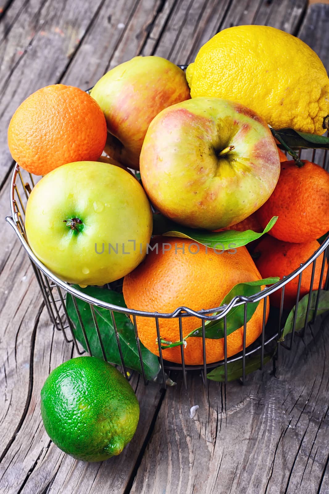 Metal fruit basket with apples and citrus fruits on the wooden table