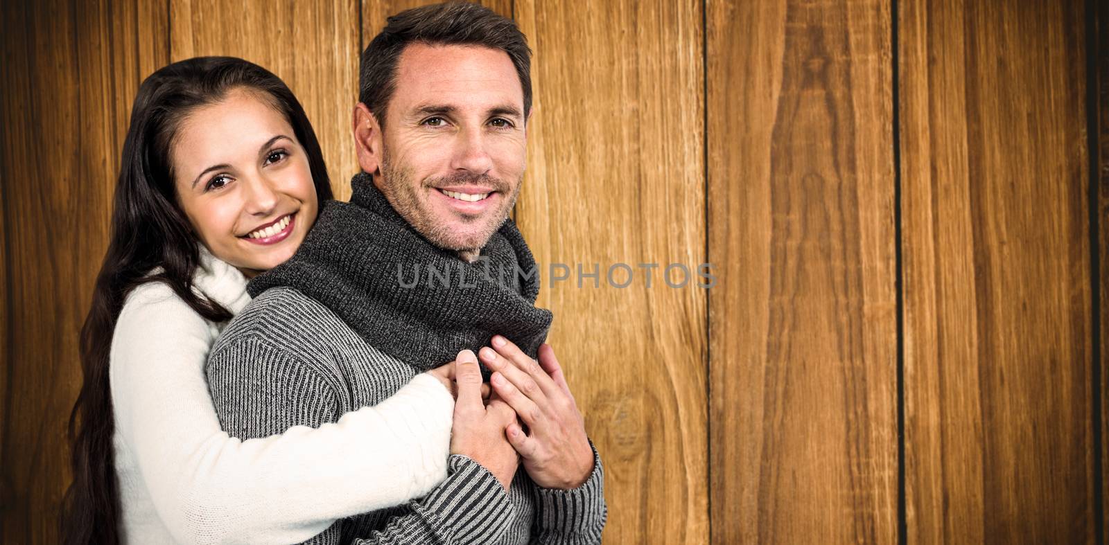 Smiling couple hugging and looking at camera against wooden background