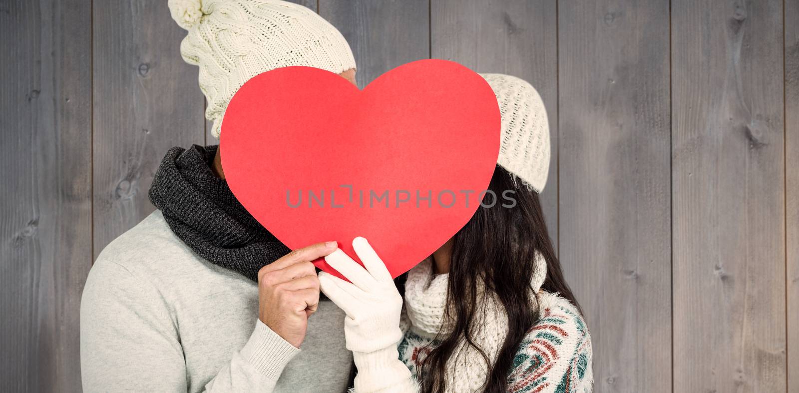Smiling couple holding paper heart against wooden planks