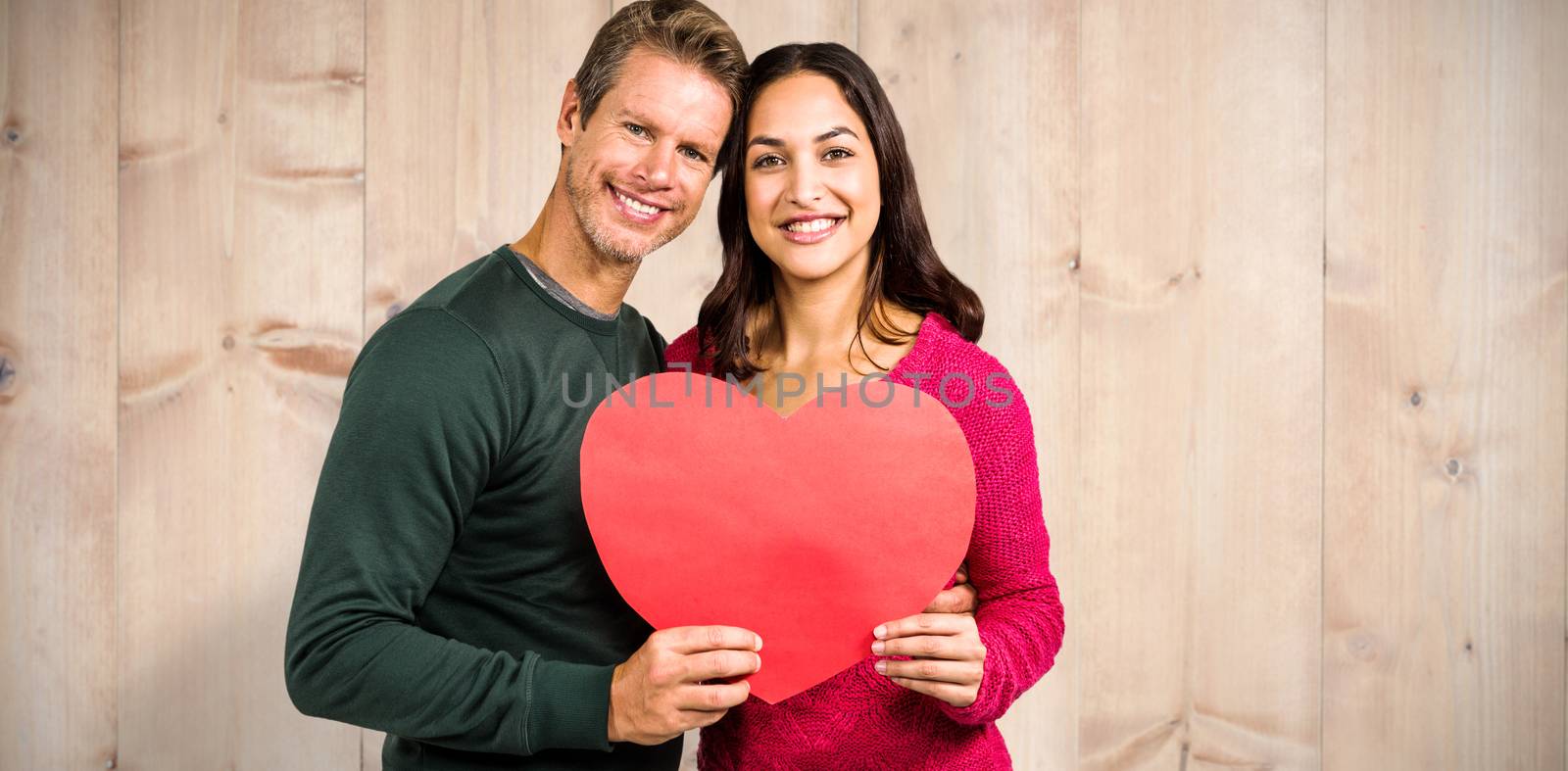Portrait of smiling couple holding heart shape against wooden planks