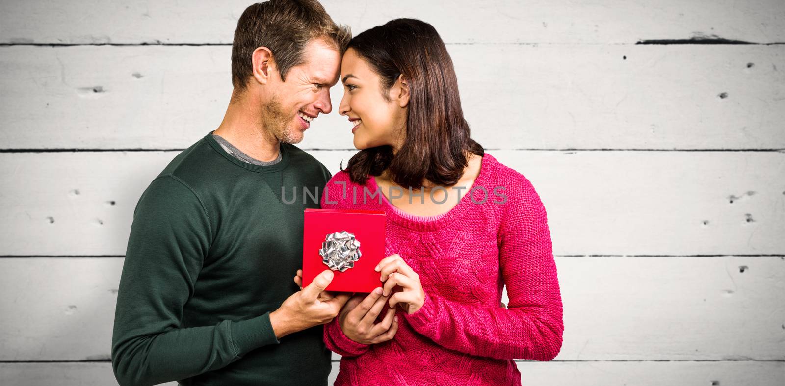 Happy couple holding gift box  against white wood