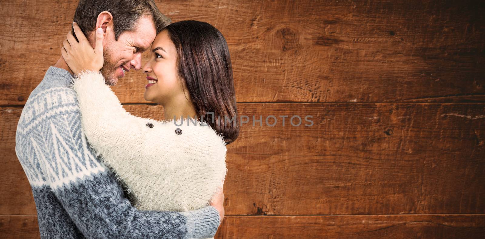 Cheerful couple in warm clothing embracing each other against overhead of wooden planks