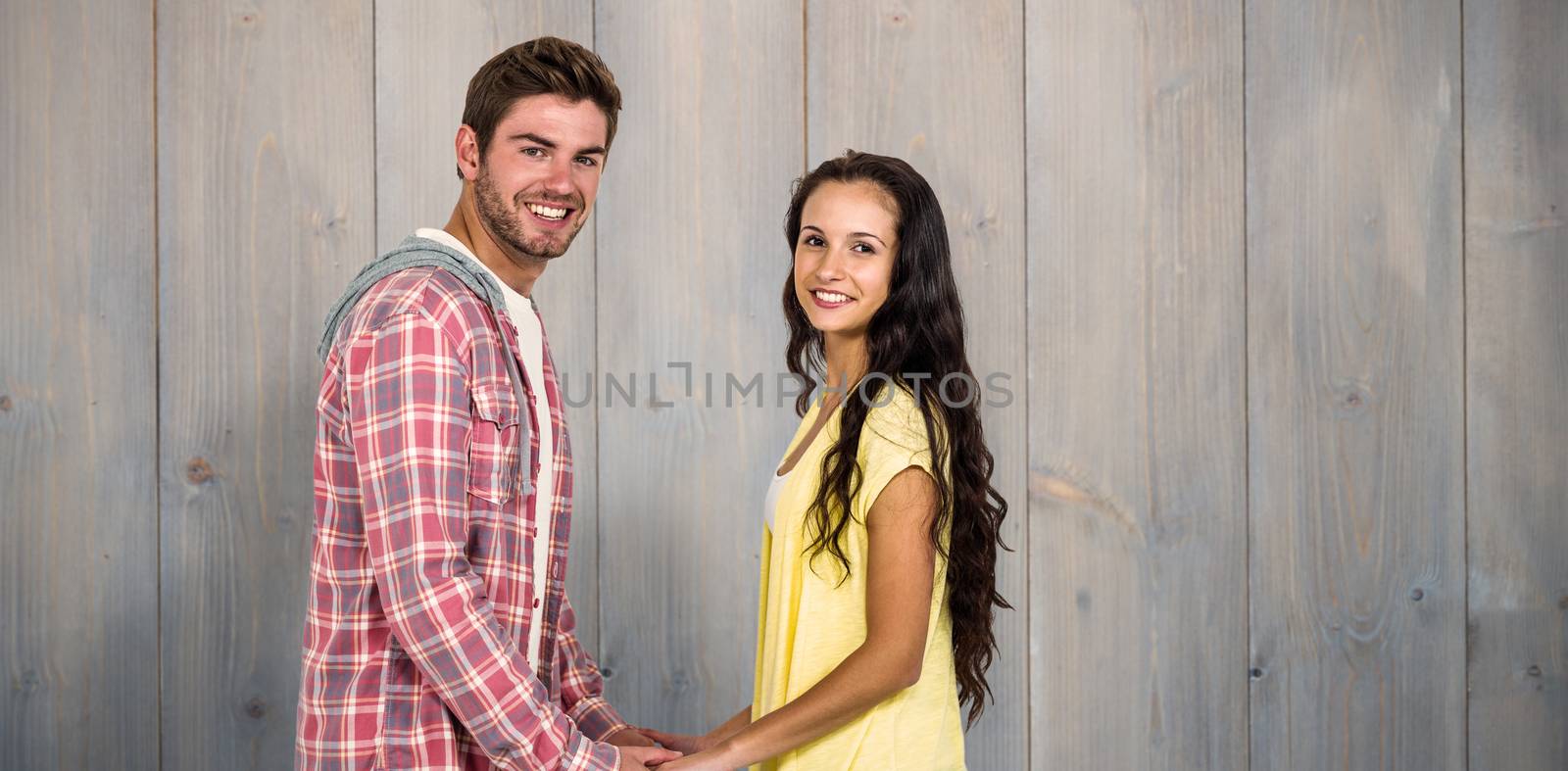 Smiling couple holding their hands and looking at camera against pale grey wooden planks