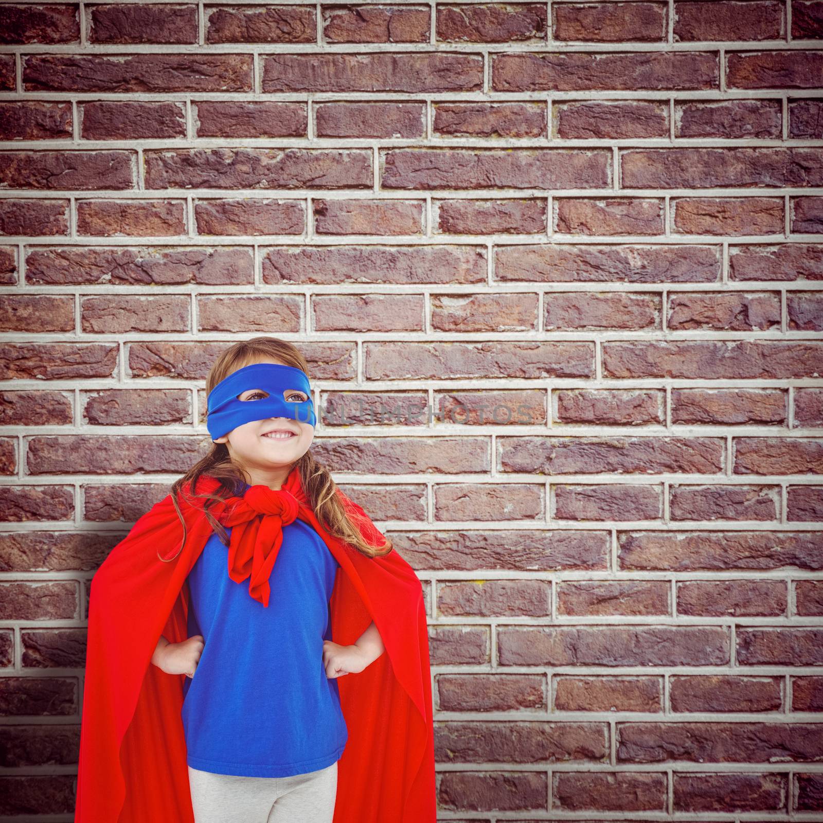 Masked girl pretending to be superhero against red brick wall