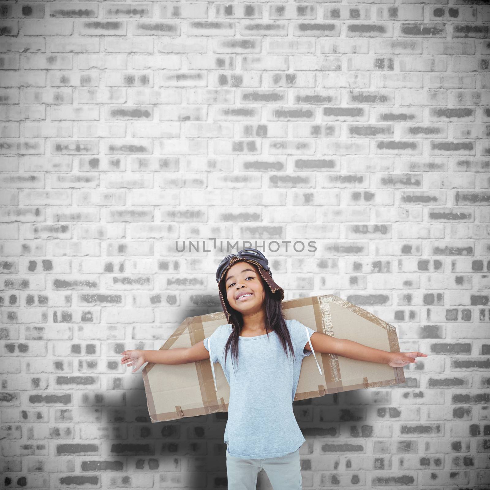 Girl with fake wings pretending to be pilot against grey brick wall