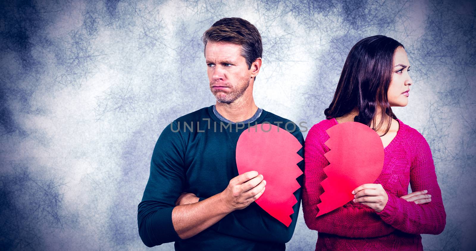 Serious couple holding cracked heart shape against grey background