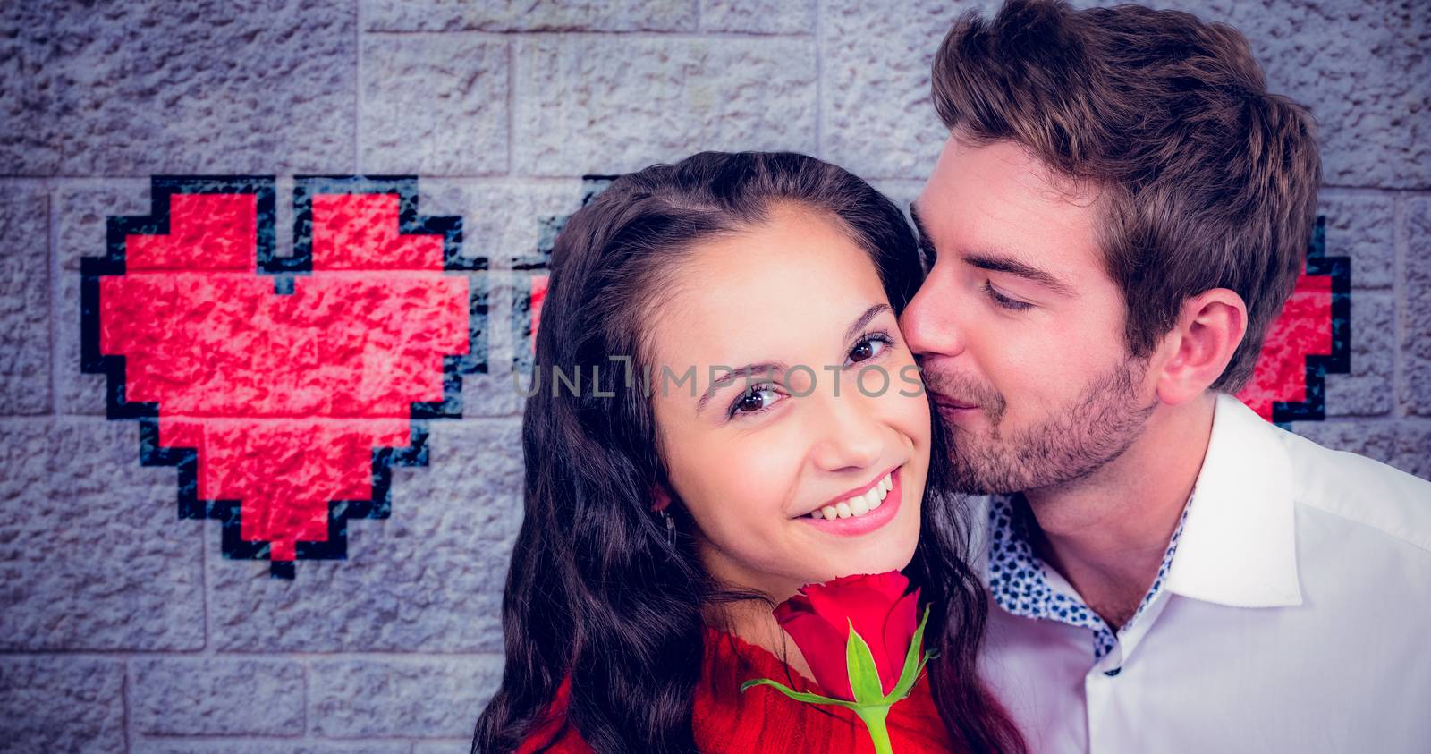 Smiling couple holding rose against grey brick wall