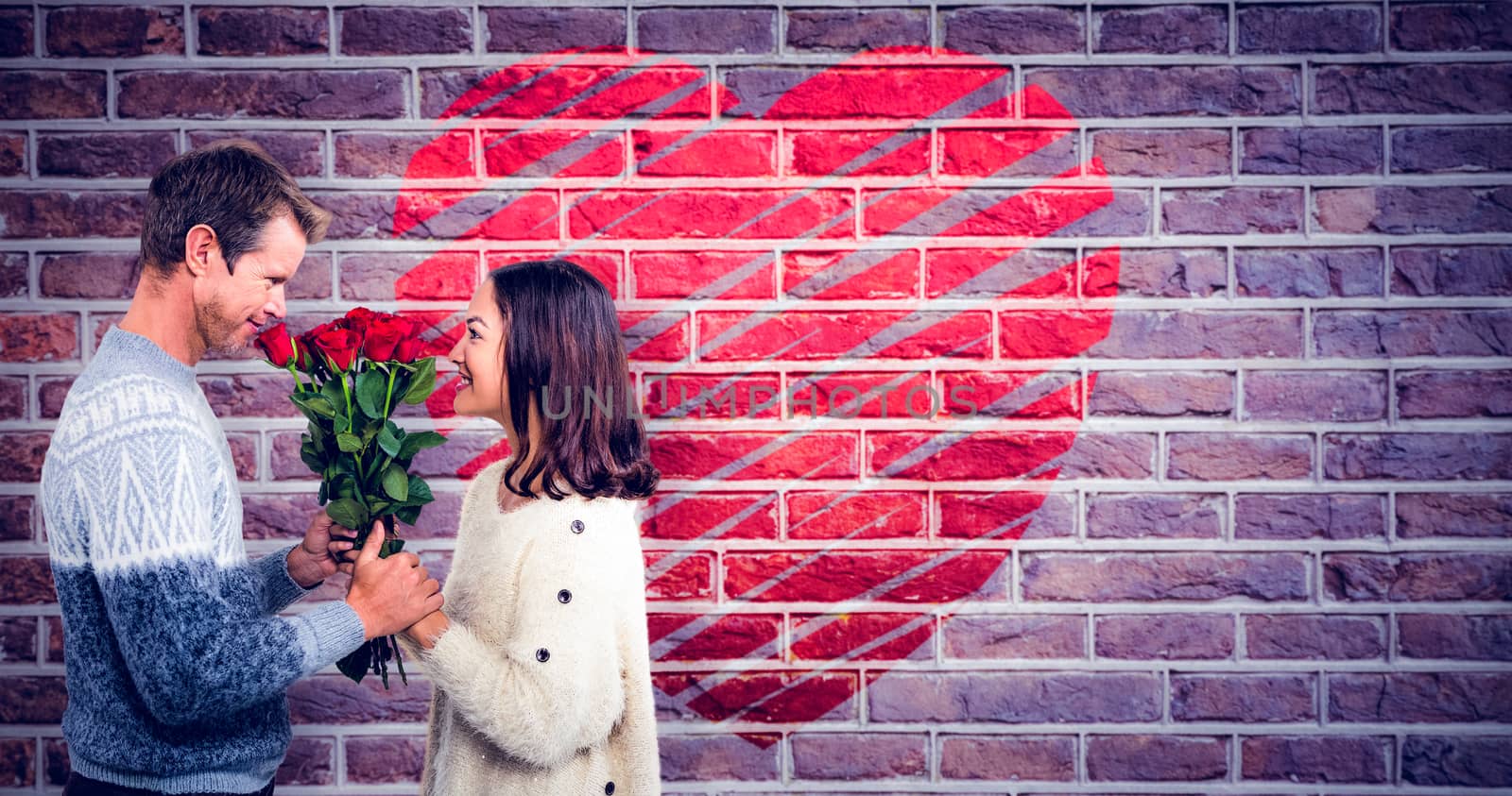 Romantic couple holding red roses against red brick wall