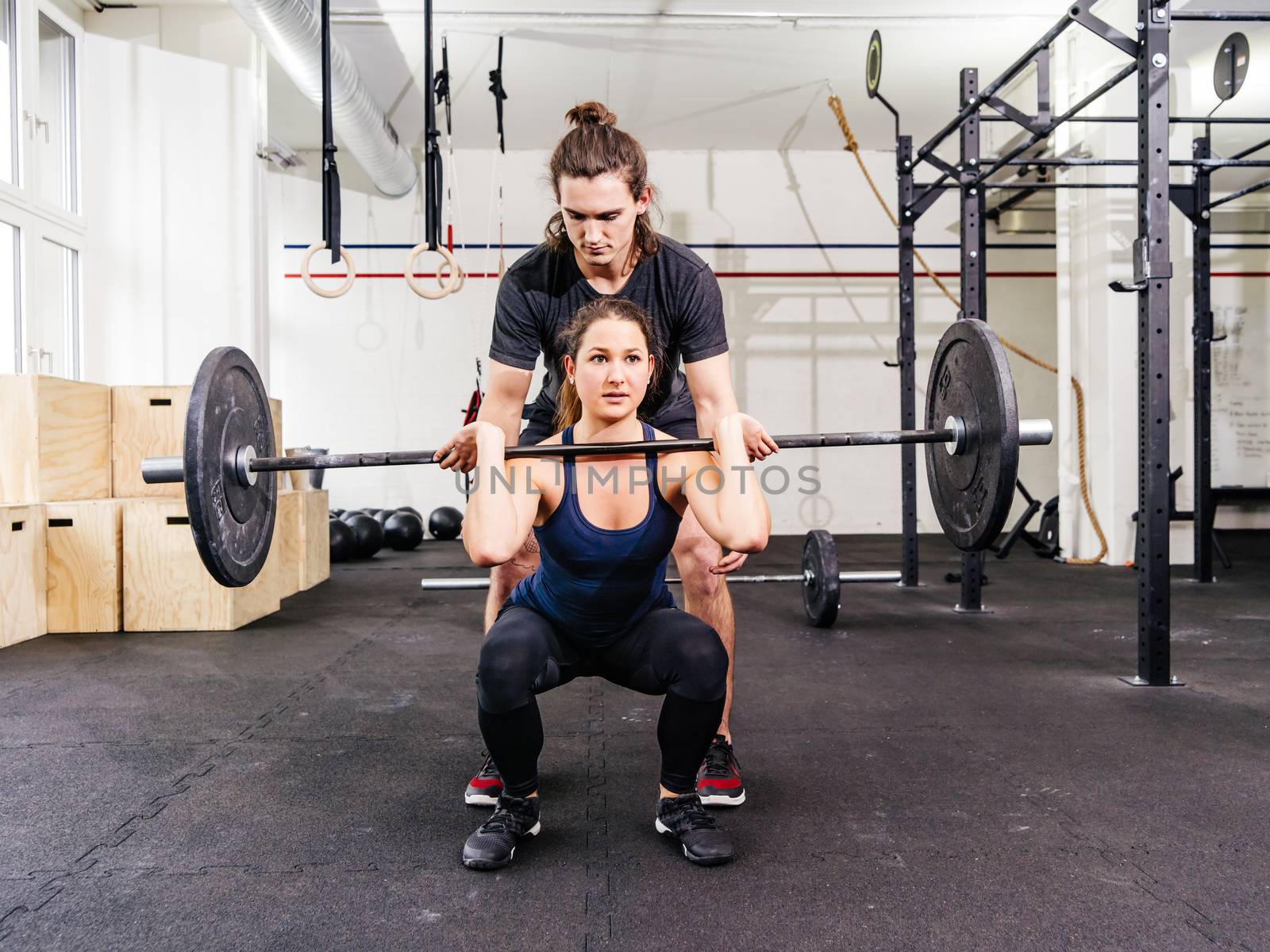 Photo of a young woman at a crossfit gym doing squats while her instructor watches from behind.