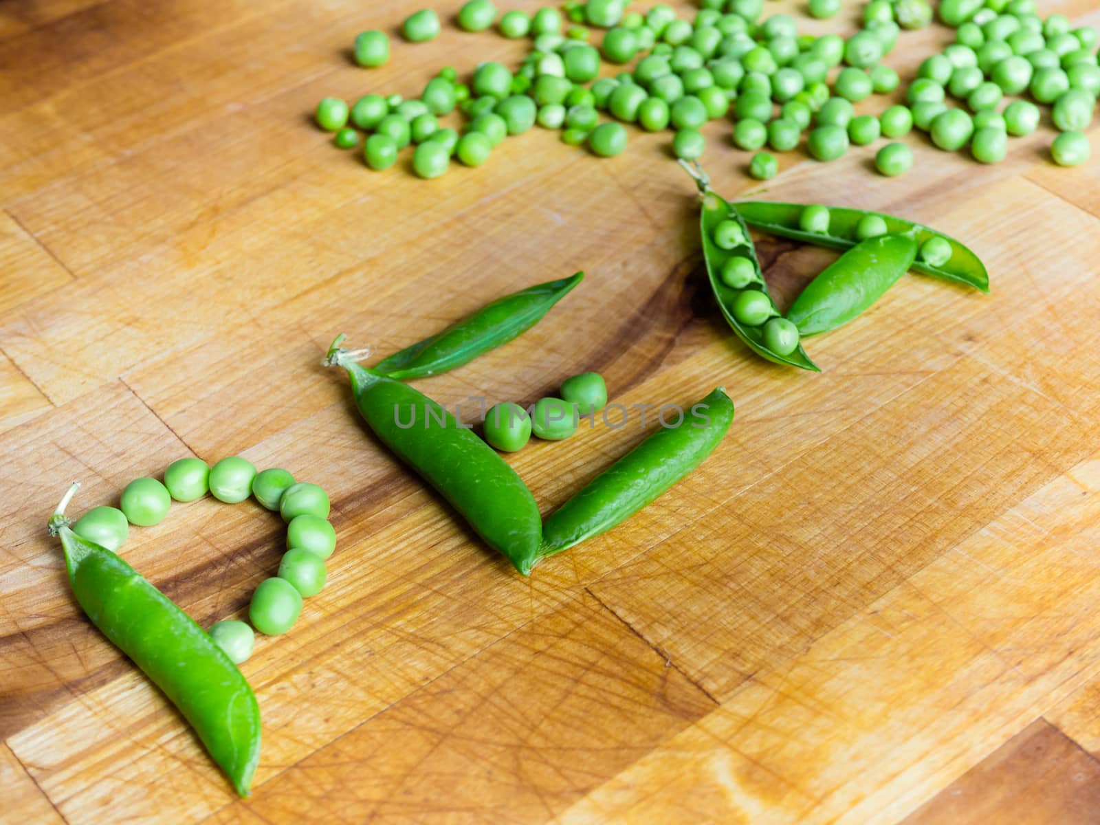 Word PEA created with peas on a wooden board with a podded peas in the background