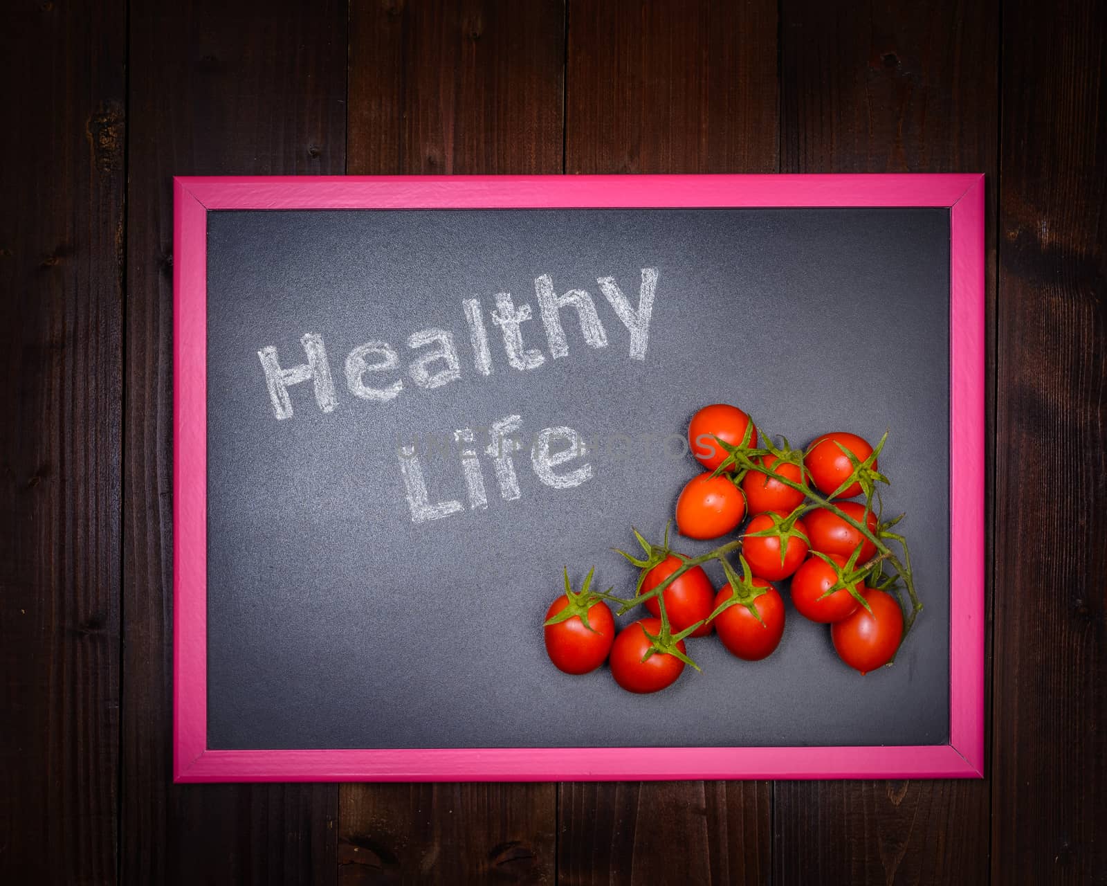 In the picture a blackboard, on the left side with written "Healthy Life" and on the right side a cherry tomato on wooden background