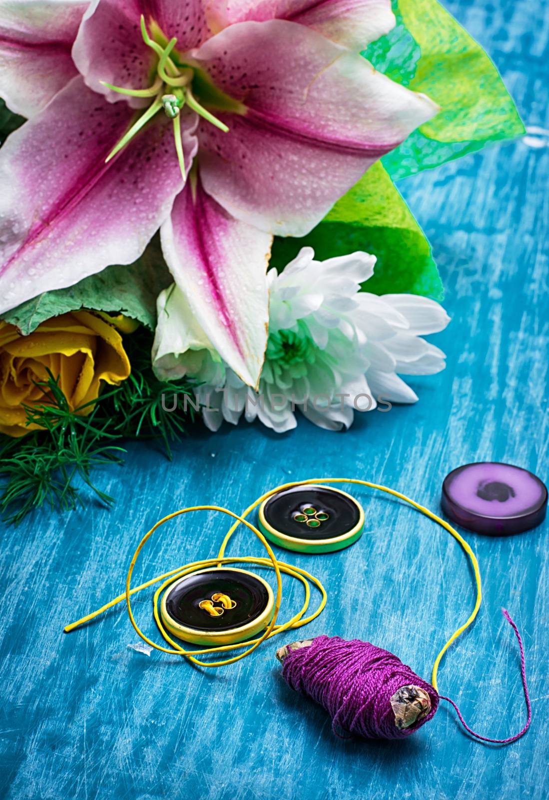sewing accessories with a bouquet of fresh flowers on turquoise background