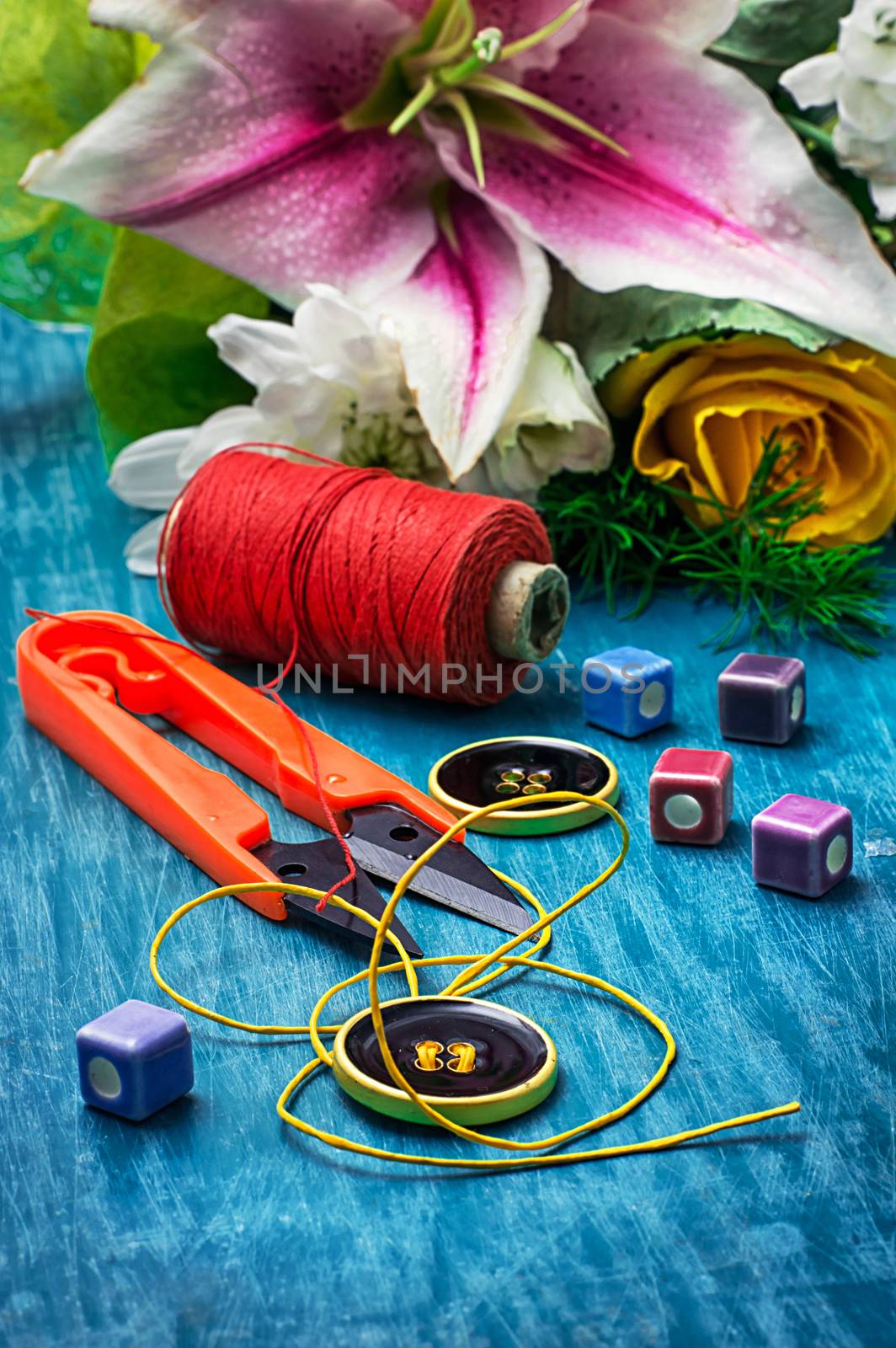 sewing accessories with a bouquet of fresh flowers on turquoise background