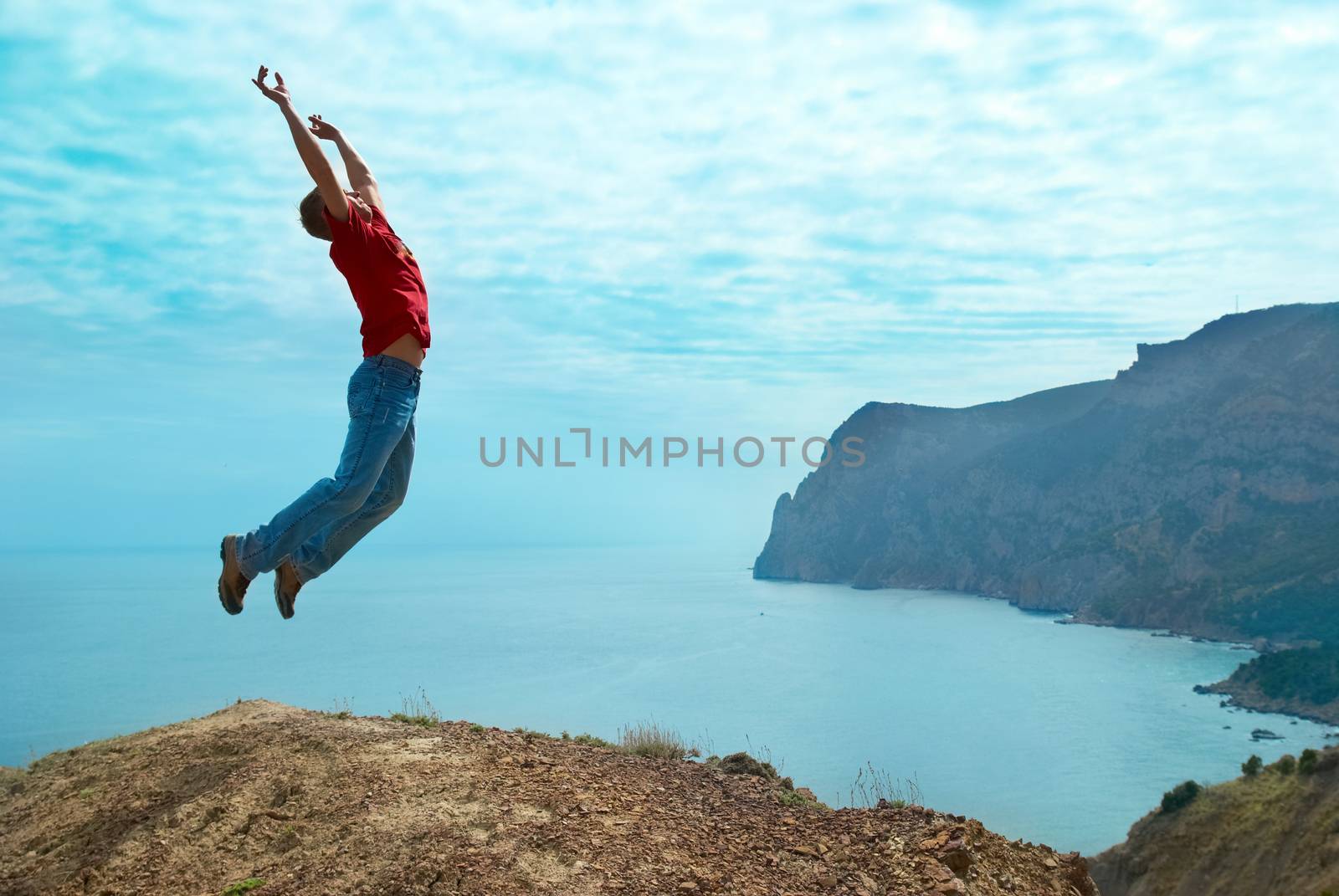 Man jumping cliff against sea and mountain with blue sky