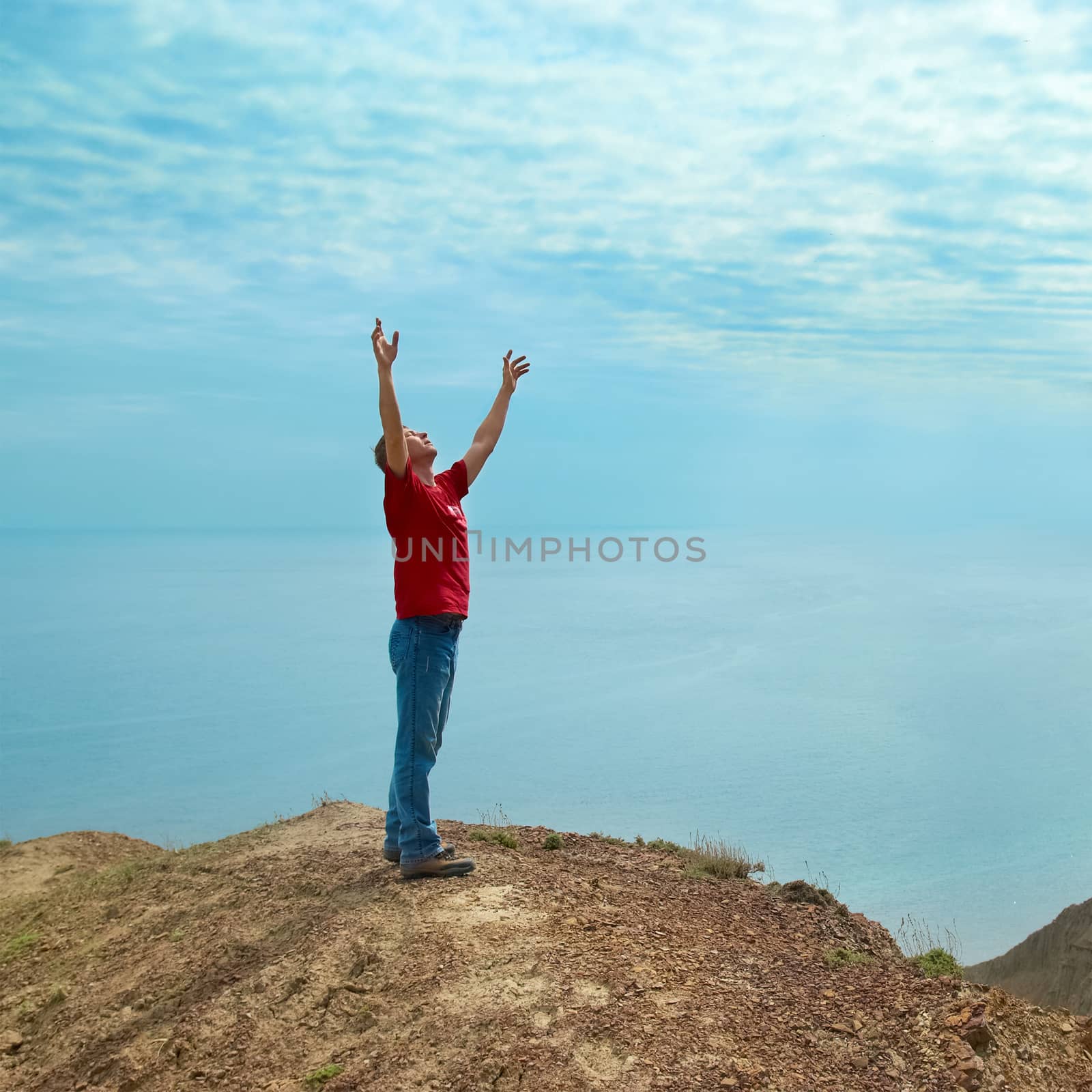 Happy man standing on the cliff with hands up looking at the sea