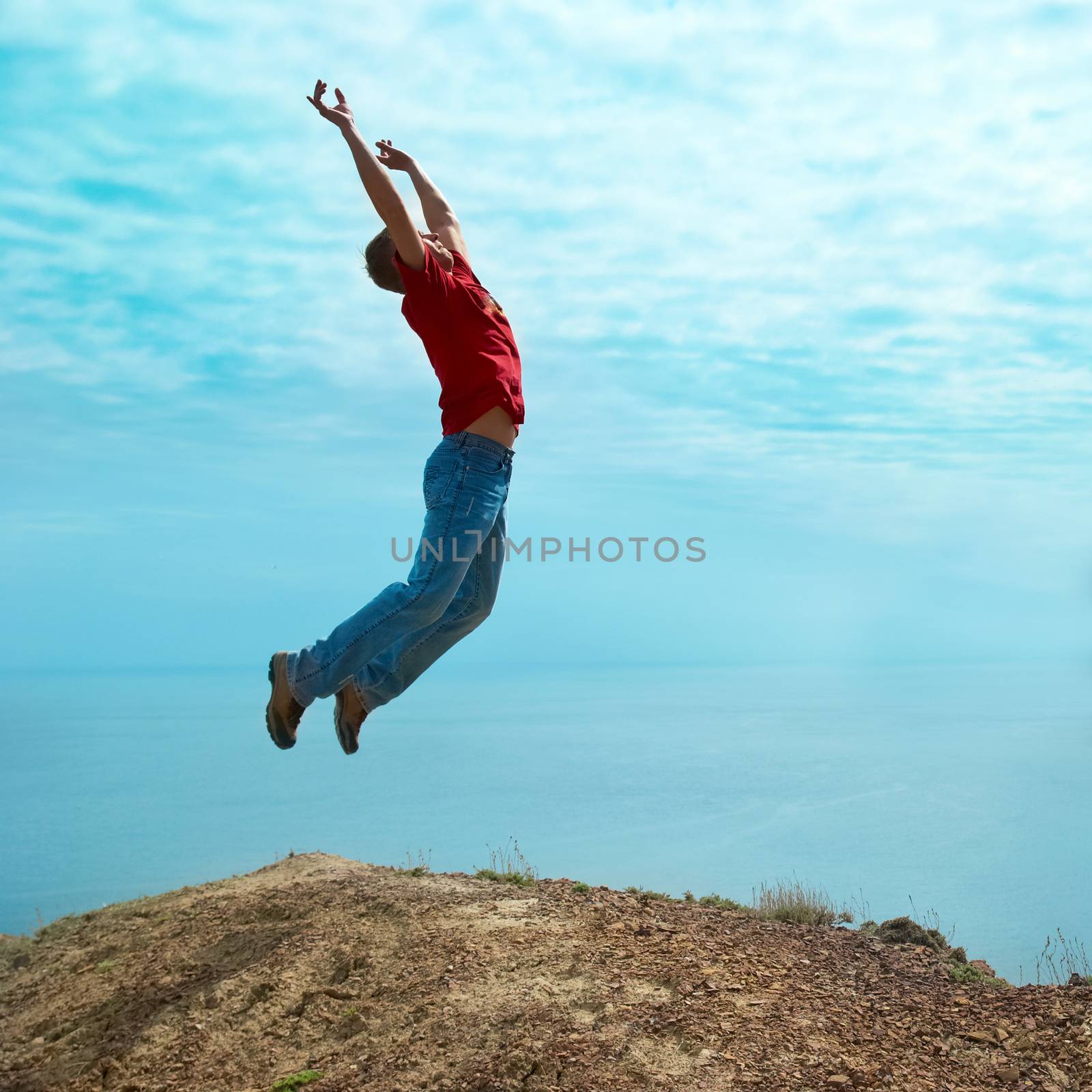 Man jumping cliff against sea and mountain with blue sky