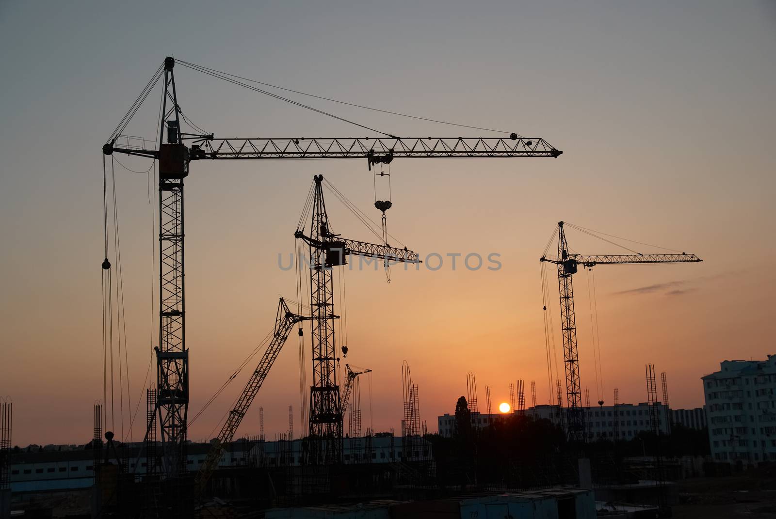 Industrial landscape with silhouettes of cranes on the sunset background