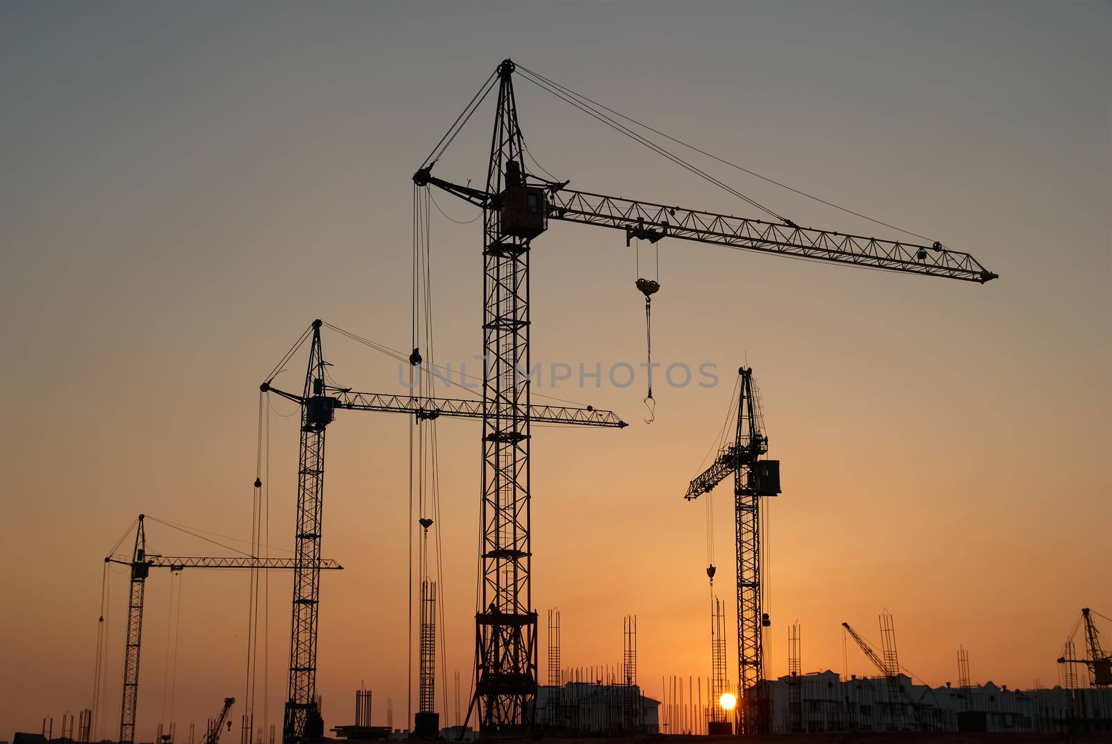 Industrial landscape with silhouettes of cranes on the sunset background