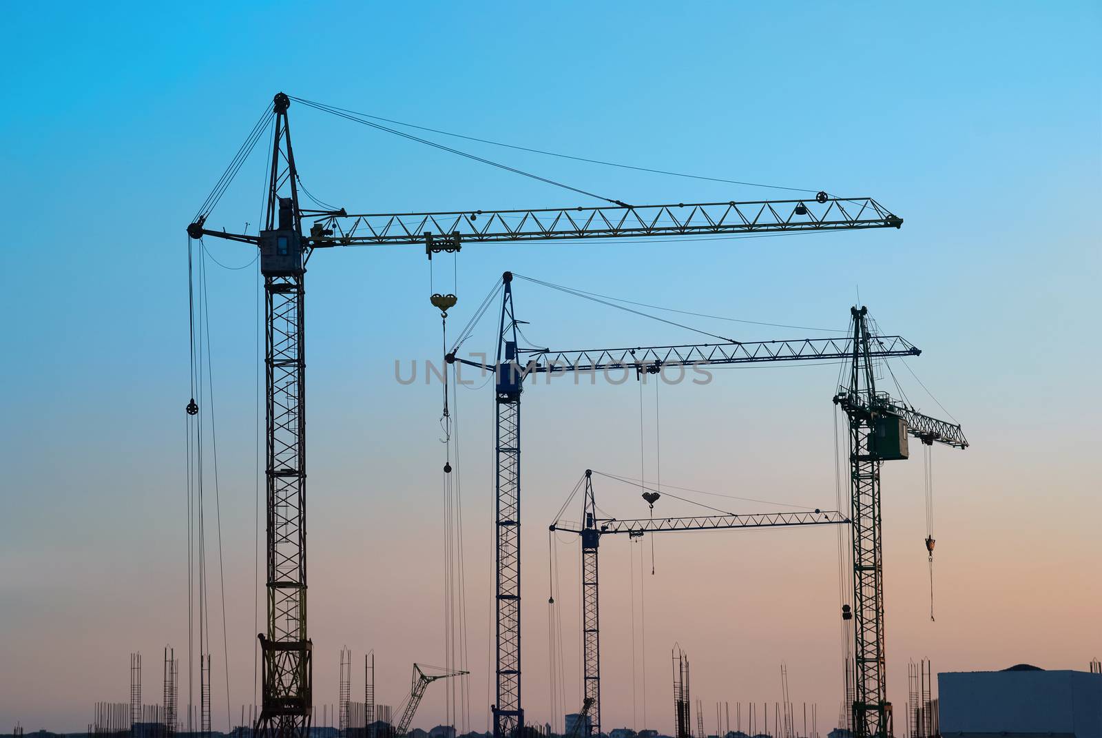 Industrial landscape with silhouettes of cranes on the sunset background