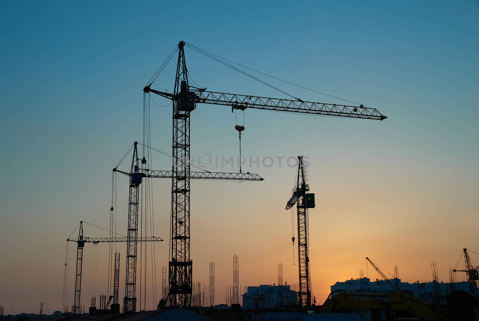 Industrial landscape with silhouettes of cranes on the sunset background