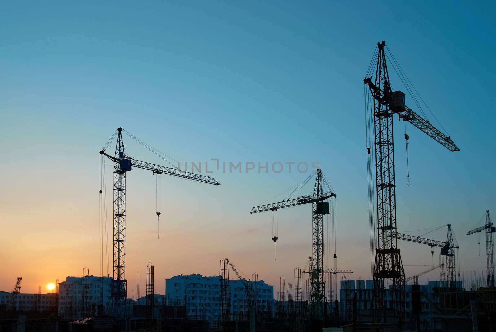 Industrial landscape with silhouettes of cranes on the sunset background