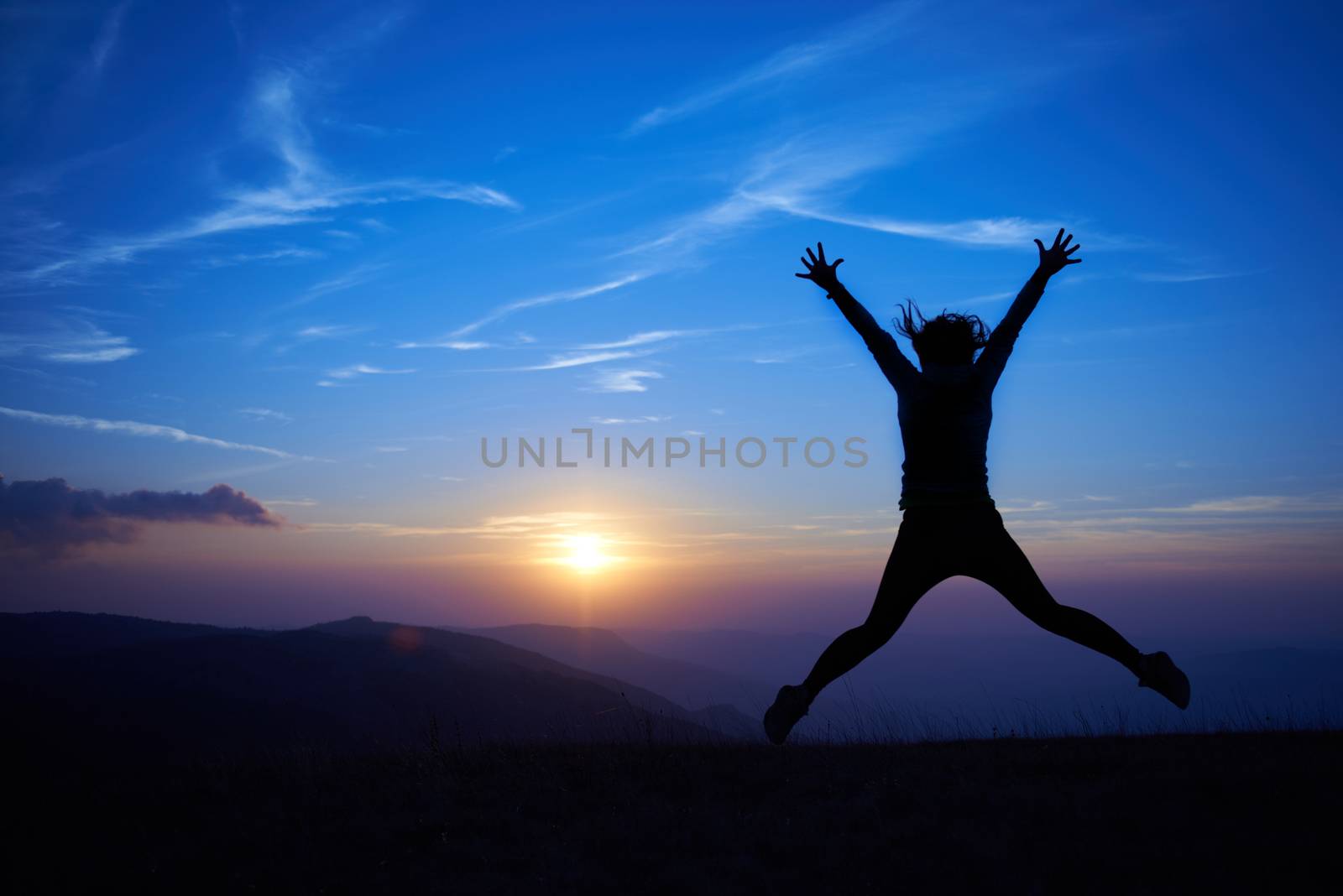 Silhouette of young woman jumping against sunset