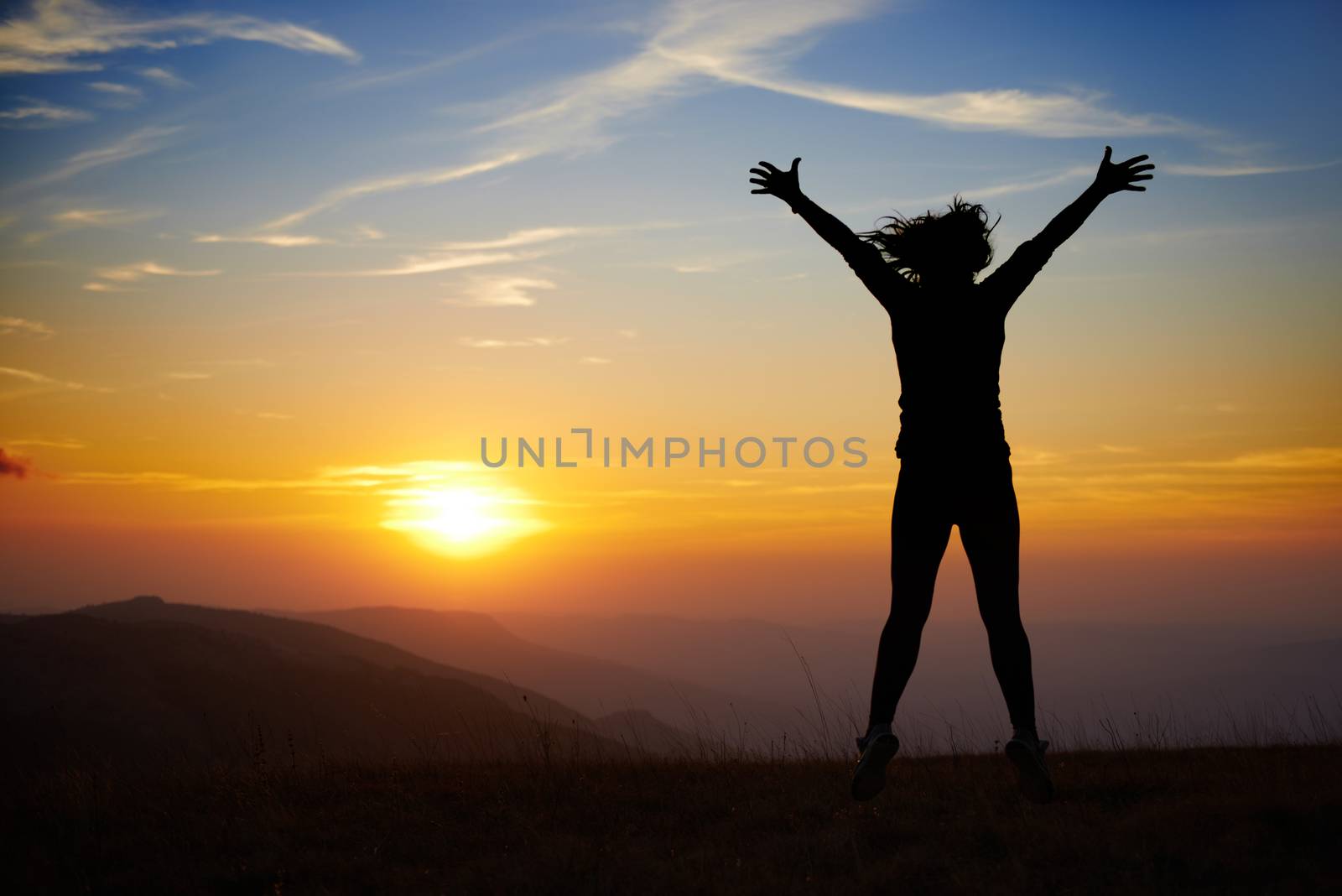 Silhouette of young woman jumping against sunset with blue sky