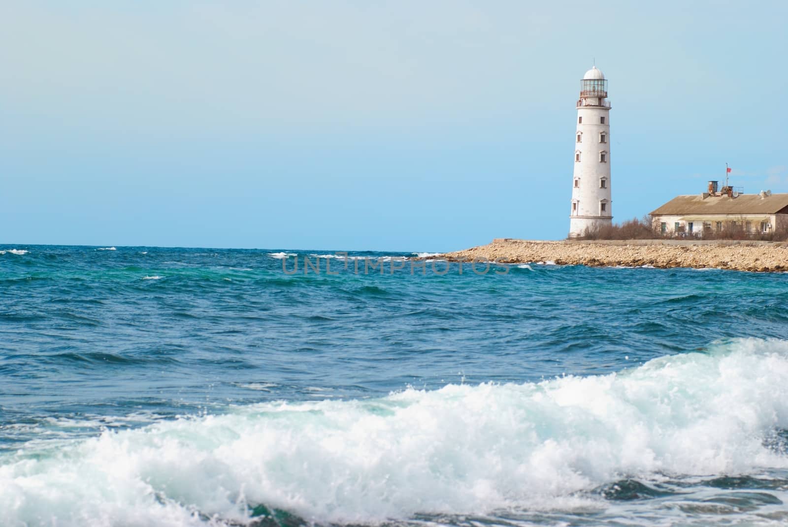 Old lighthouse on the sea coast. Storm, waves and blue sky.