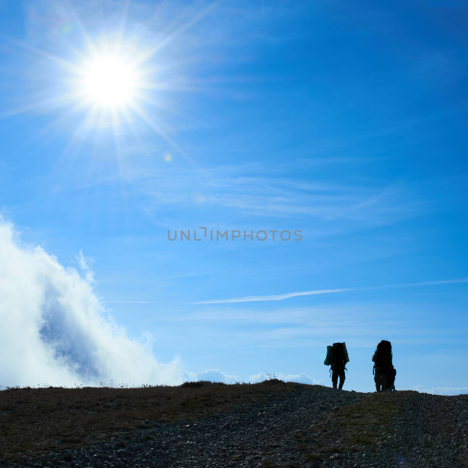 Silhouette of hiking friends against sun and blue sky