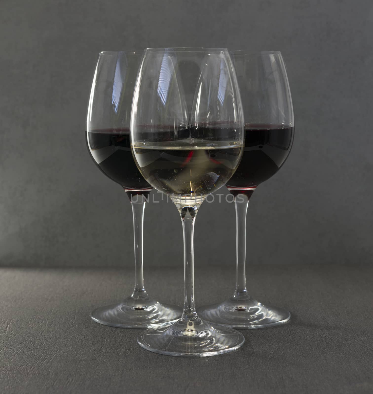 one glass white wine in front of two glasses red wine